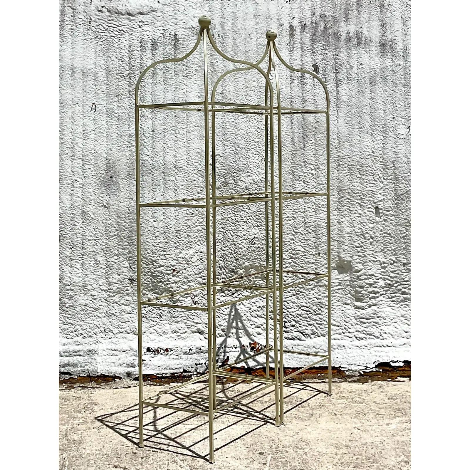 Fabulous pair of vintage wrought iron etagere. Beautiful Regency design with a chic peak design. Currently an off white, but easily changed to any color that works for you. Inset glass shelves. Acquired from a Palm Beach estate.