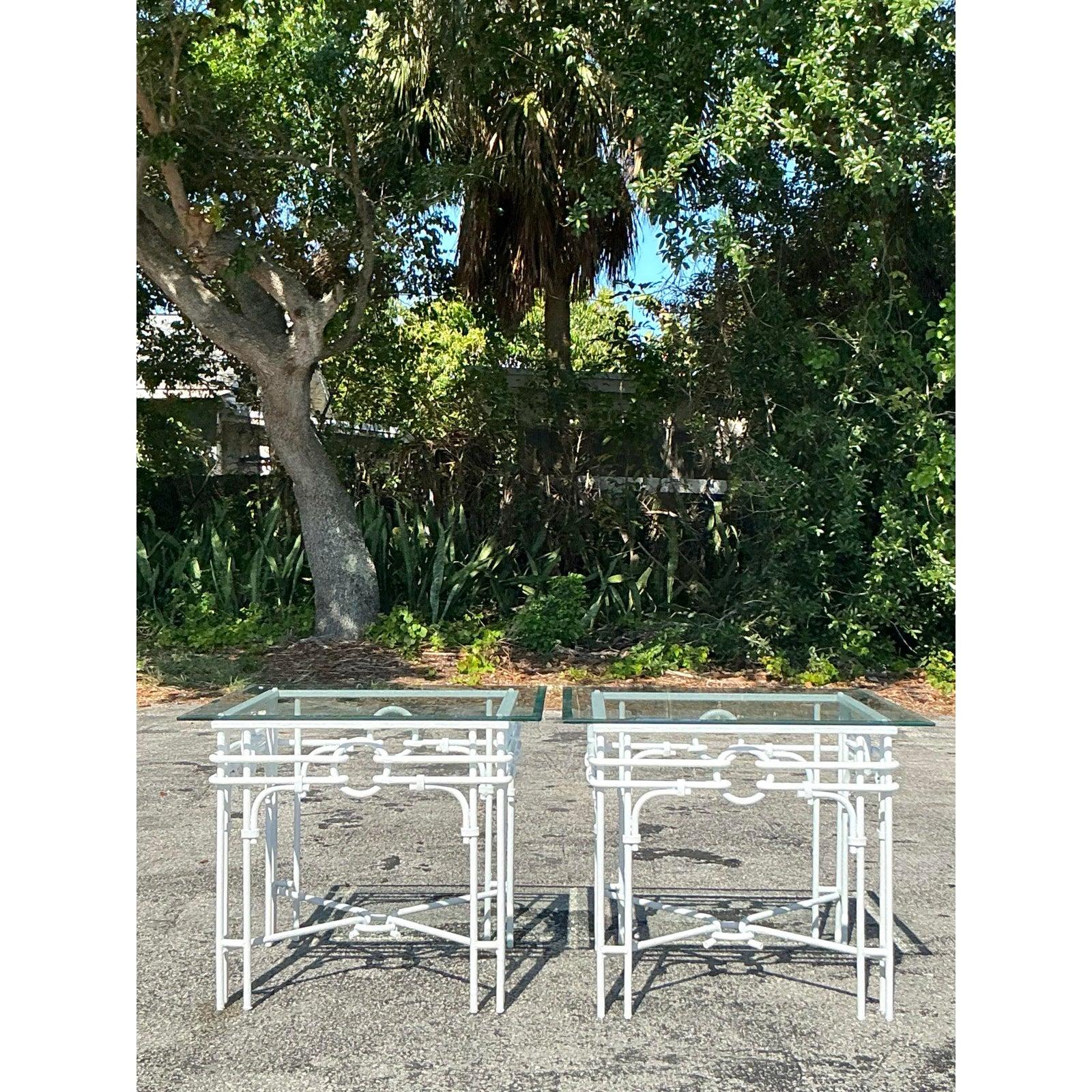 Verleihen Sie Ihrem Raum einen Hauch von Palm Beach-Flair mit diesem eleganten Paar schmiedeeiserner Beistelltische im Regency-Stil. Mit ihren verschnörkelten, kreisförmigen Motiven, der strahlend weißen Oberfläche und den glatten Glasplatten