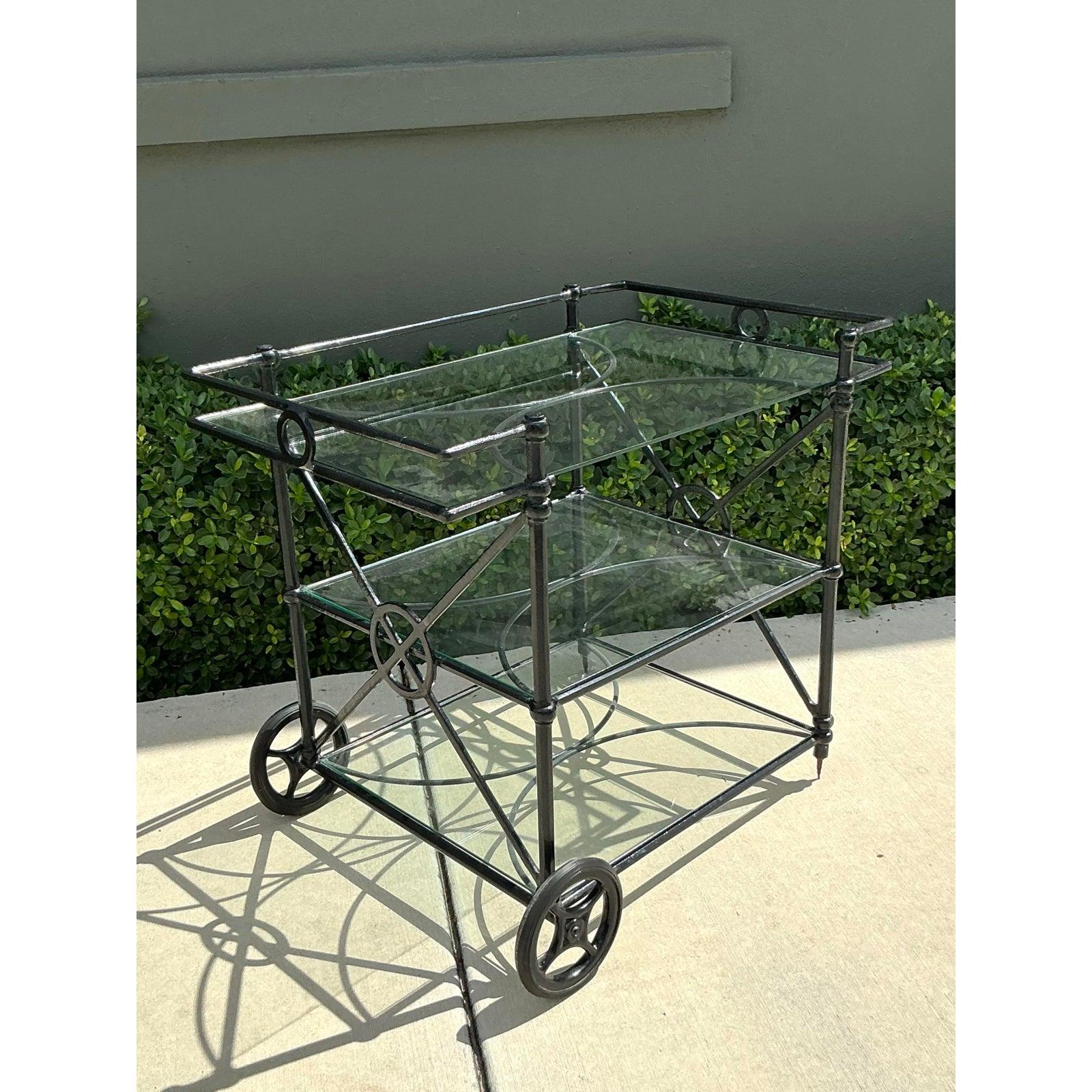 Presenting a stylish Vintage Hollywood Regency Wrought Iron & Glass Bar Cart, originally retailed by Target. This elegant dry bar embodies the glamorous aesthetic of the Hollywood Regency era, featuring a sophisticated black wrought iron frame with