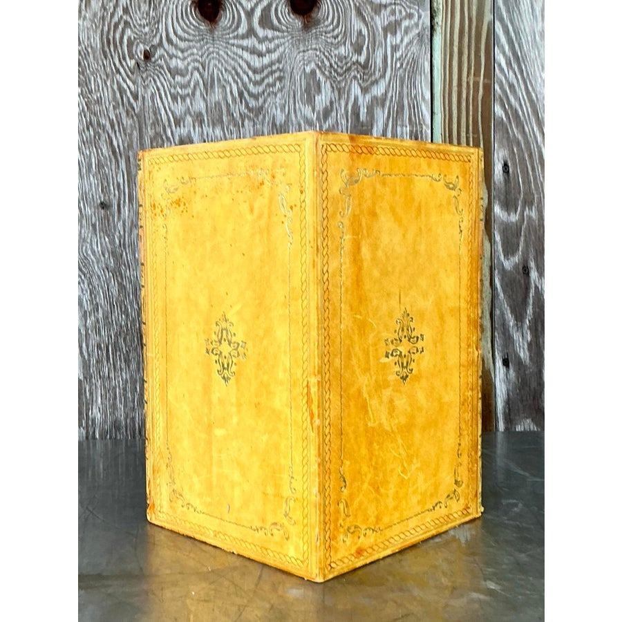 Trasforma il tuo spazio con il fascino vintage di questo cestino per libri in rilievo giallo Regency. Progettato per imitare un classico libro rilegato in pelle, questo pezzo unico presenta intricati dettagli impressi in oro che evocano la