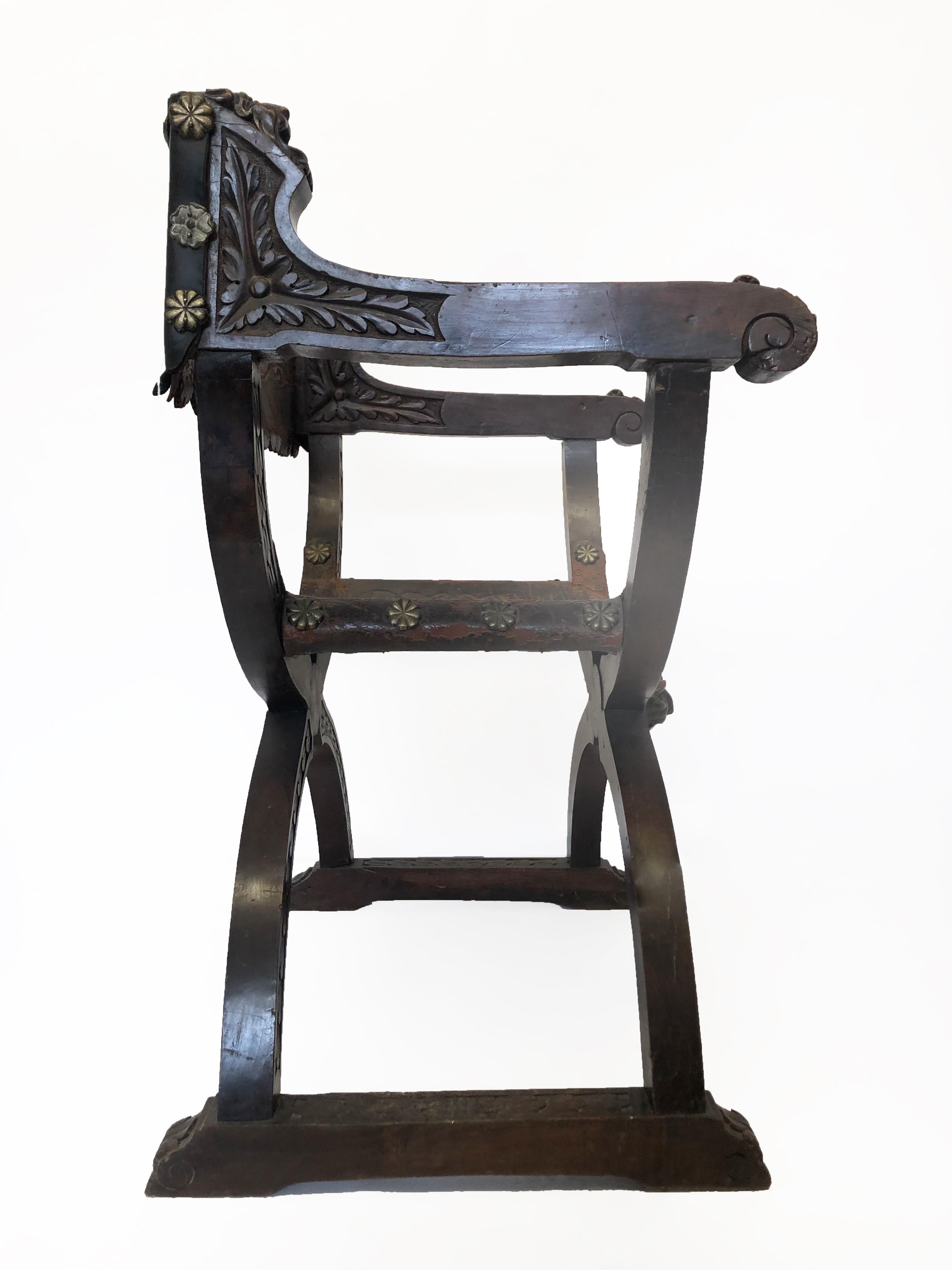 This is a Dante or Savonarola wood and leather settle chair. The wood work is an X- shaped frame with leather back and seating. The entire chair is adorned with carvings throughout its scrolled arms rests, and highly detailed over the back frame and