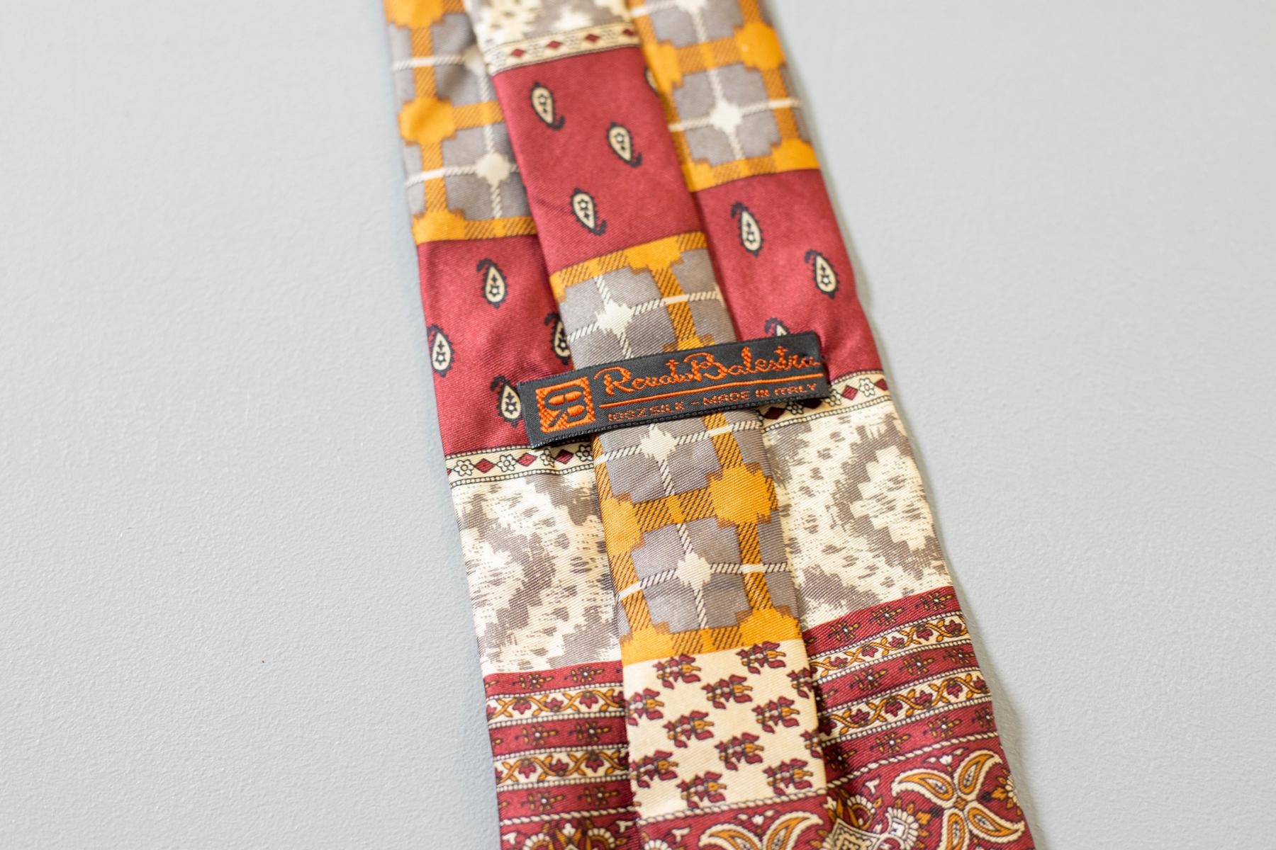 Questa eccentrica cravatta disegnata da Renato Balestra è realizzata interamente in seta. Colorata ed estremamente decorata, questa cravatta presenta motivi paisley e geometrici. La parte esterna richiama tutti i colori caldi, mentre la parte