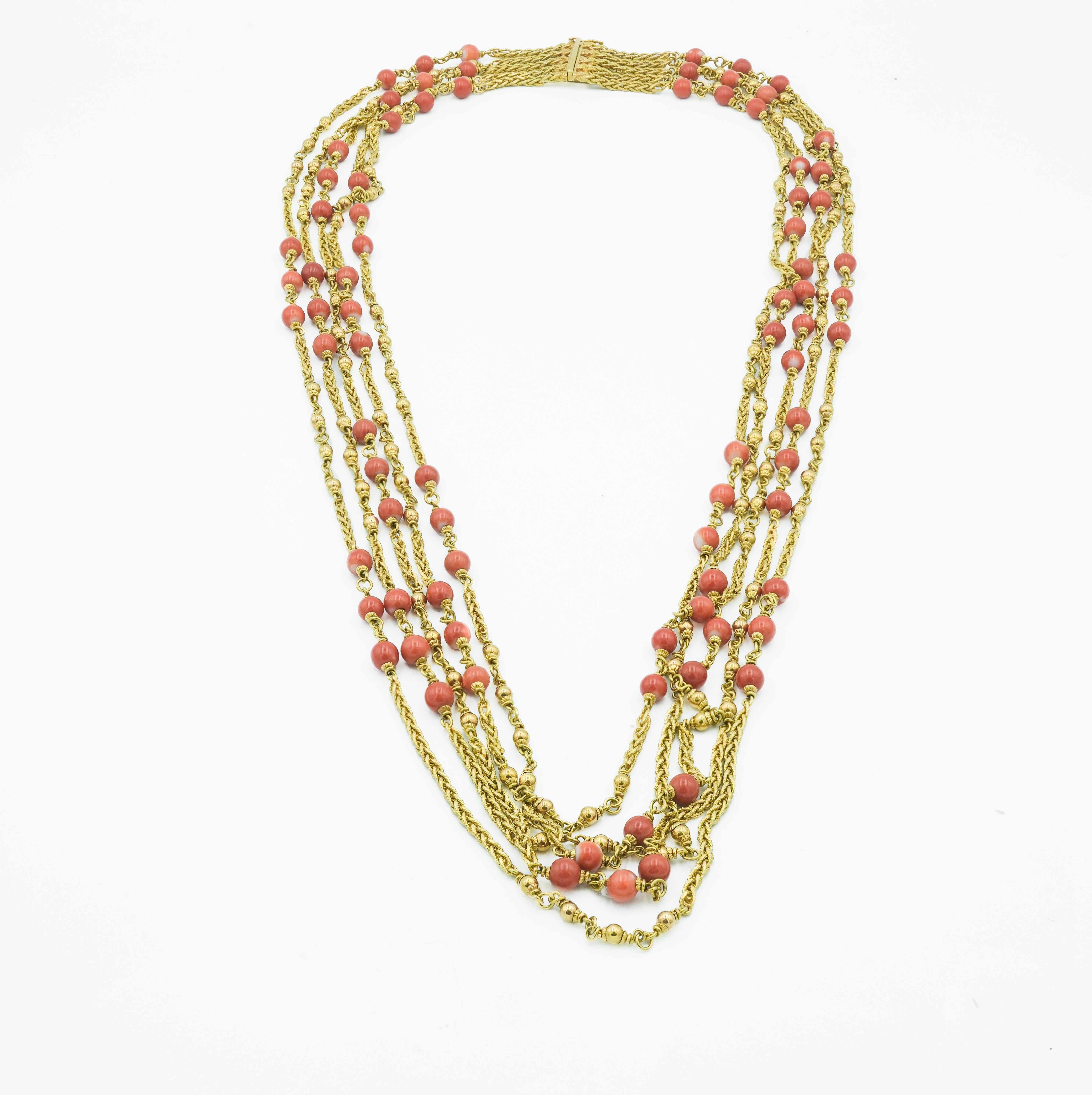Diese mehrreihige, mehrschichtige Halskette ist ein handgefertigtes Stück aus 18 Karat Gelbgold und mit Korallenperlen verziert. Das Design besteht aus mehreren Ketten, die ineinander verschlungen sind und in Kaskadenform verlaufen, wodurch ein