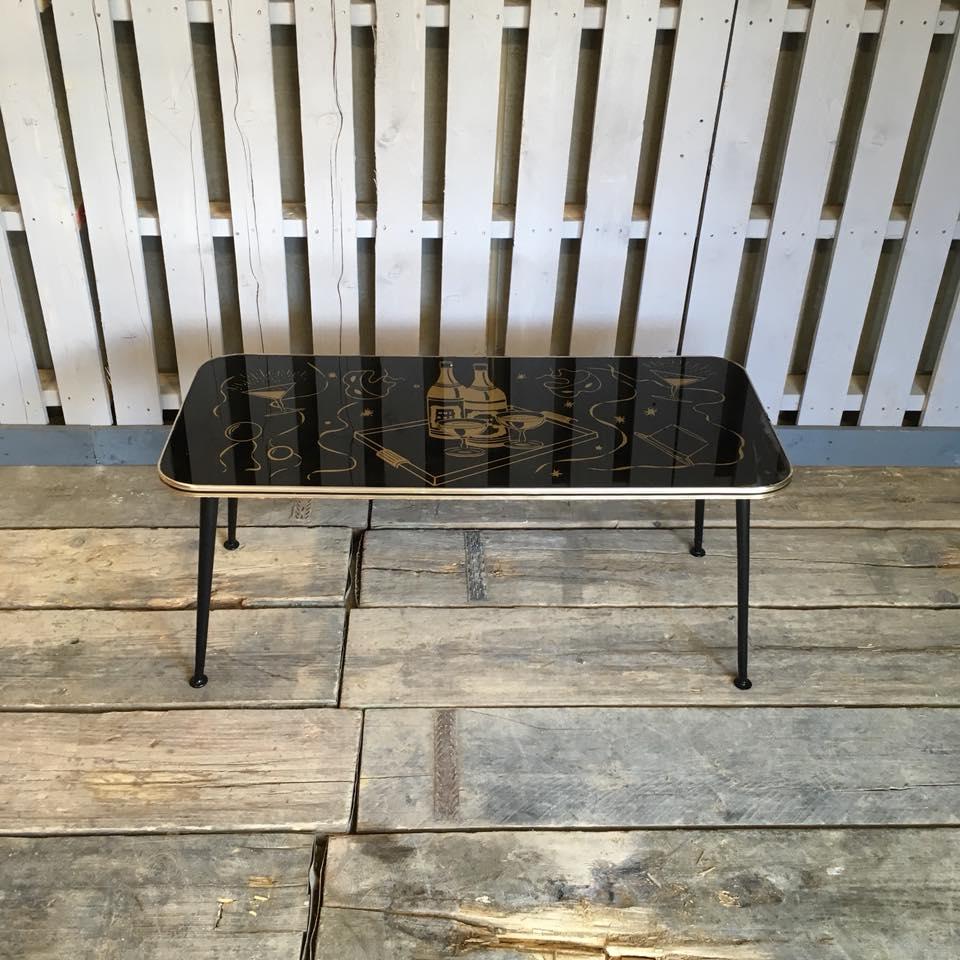 Vintage coffee table sat on dansette / atomic legs. Has a party theme on the top in gold. In good condition has some slight blooming on one corner and a slight gap in the good trim that runs around the side.