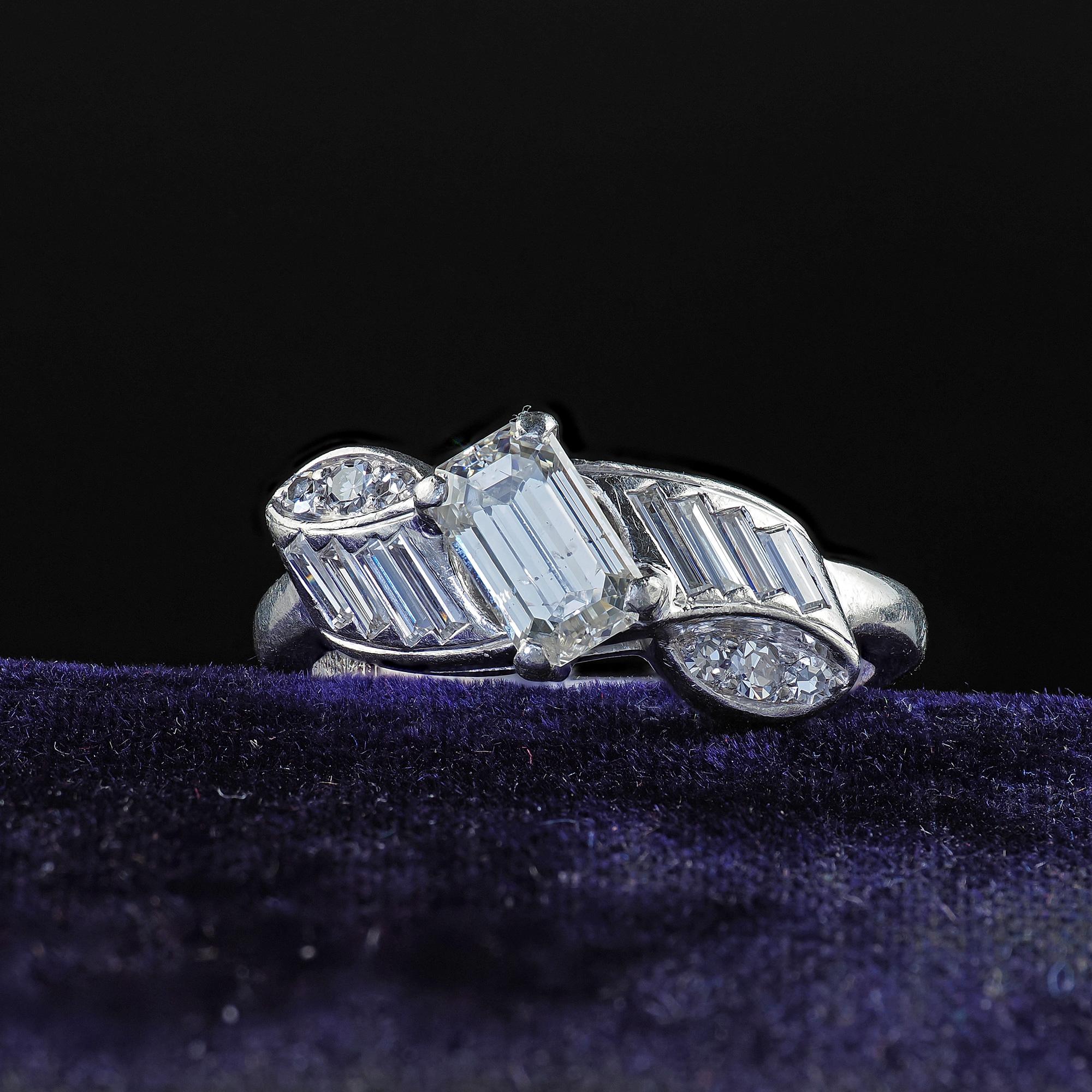 Beautiful Vintage Retro Hartzberg Platinum Emerald Cut Diamond Ribbon Engagement Ring. This gorgeous emerald cut diamond ring is crafted in platinum. The center holds an old emerald cut diamond and is surrounded by single cut diamonds and baguettes