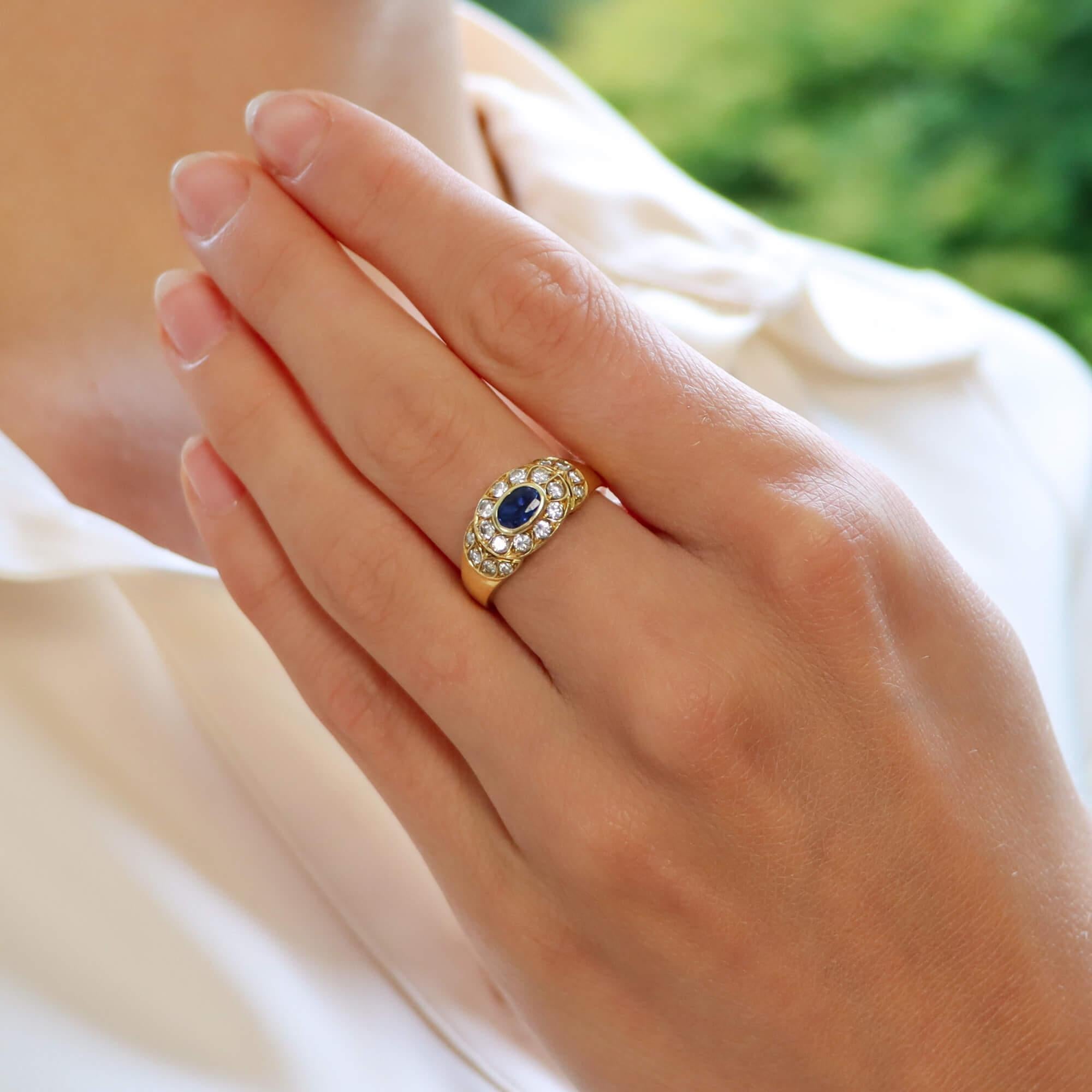 A beautiful retro inspired diamond and sapphire cluster ring set in 18k yellow gold.

This beautiful piece is centrally rub over set with an oval cut blue sapphire and is surrounded by a cluster of 10 round brilliant cut diamonds. The shoulders of