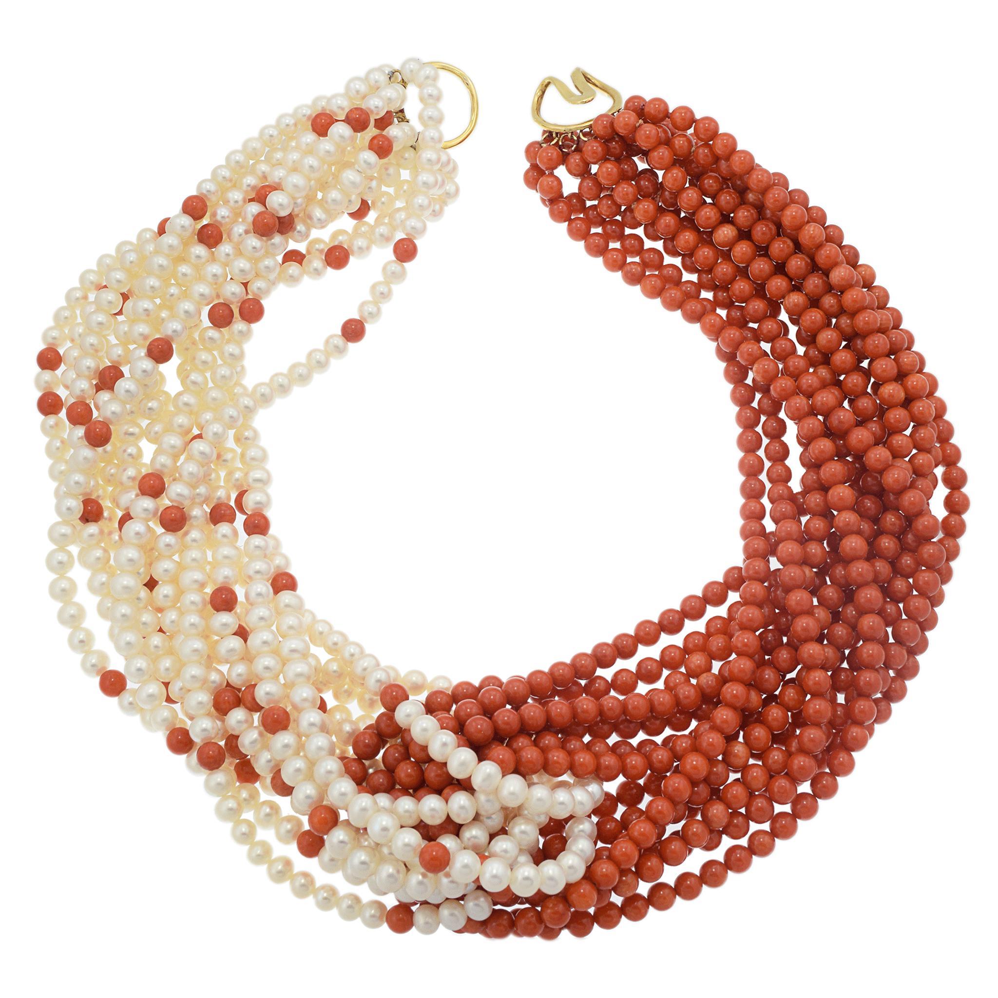 A striking coral and pearl necklace.

It features multiple strands of red coral beads, creating a bold and vibrant look. Interspersed with the coral are strands of lustrous white pearls, adding contrast and elegance.

The necklace is finished with a