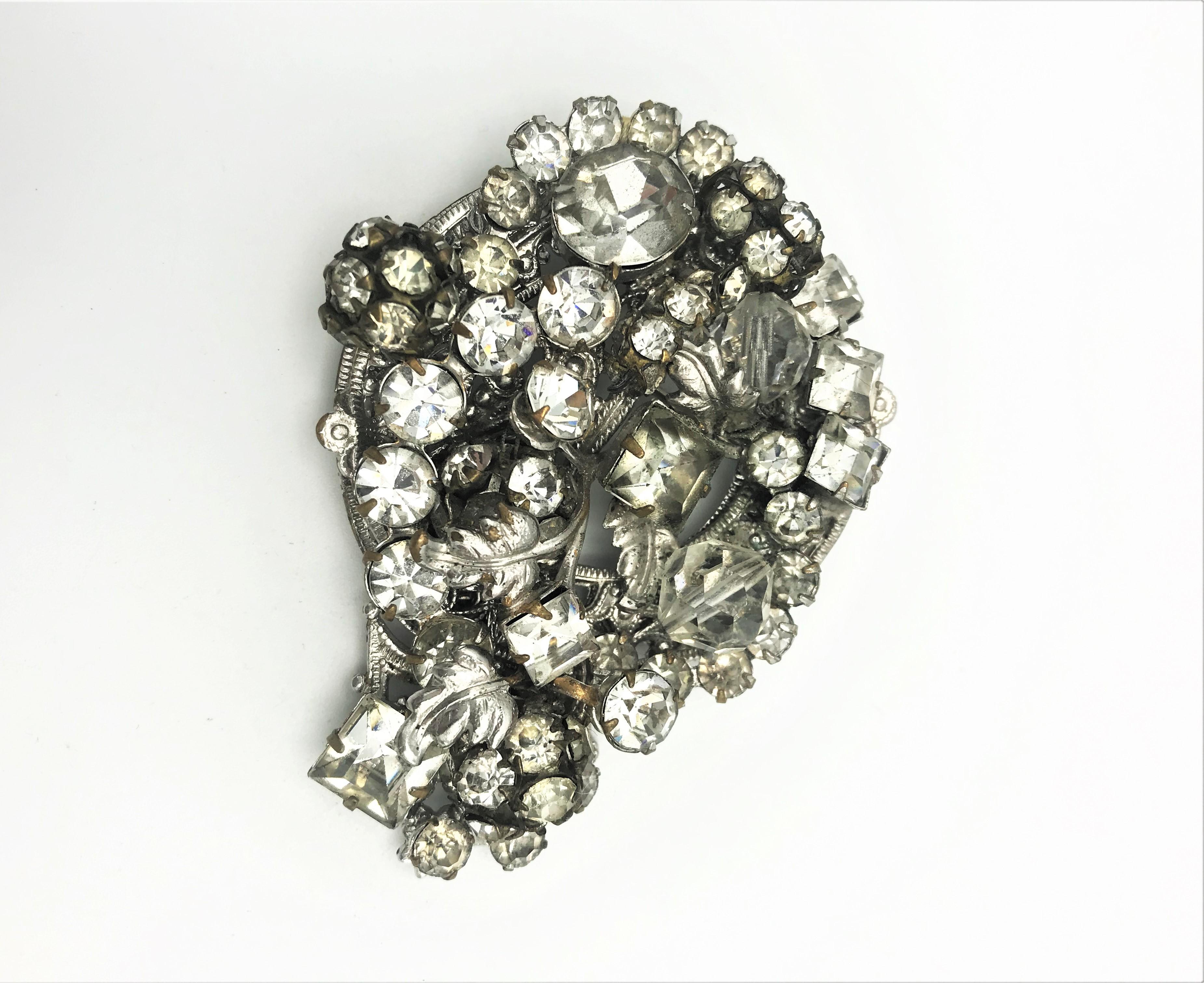 A very decorative and plastic brooch by Robert USA filled with many different sized and cut rhinestones, in between there are small silver-colored leaves.
Measurement: Height 7.5 cm, Width 4.5 cm.