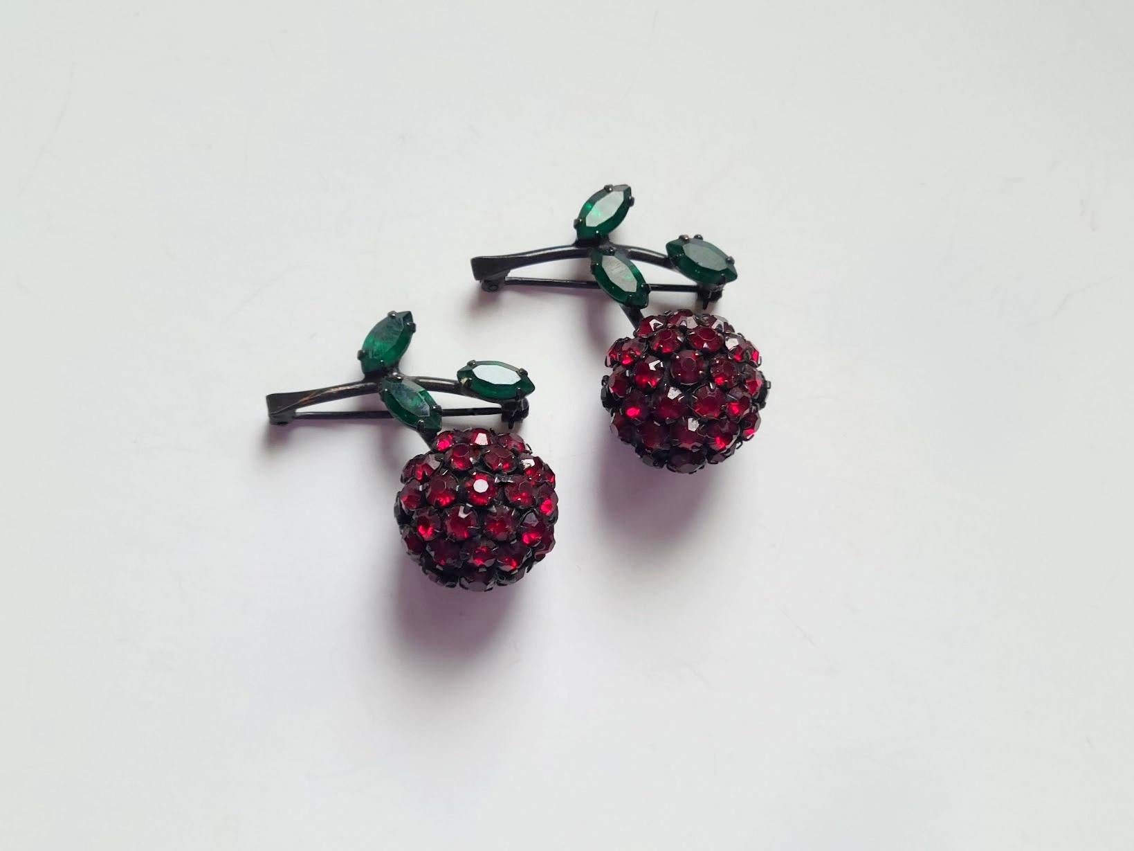 This is a two vintage rhinestone cherry brooches with green leaves from Warner, circa 1960s.
Set with garnet rhinestone chatons (the head of a ring in which a stone is set) for the cherry and green marquis cut rhinestones for the leaves on a black,