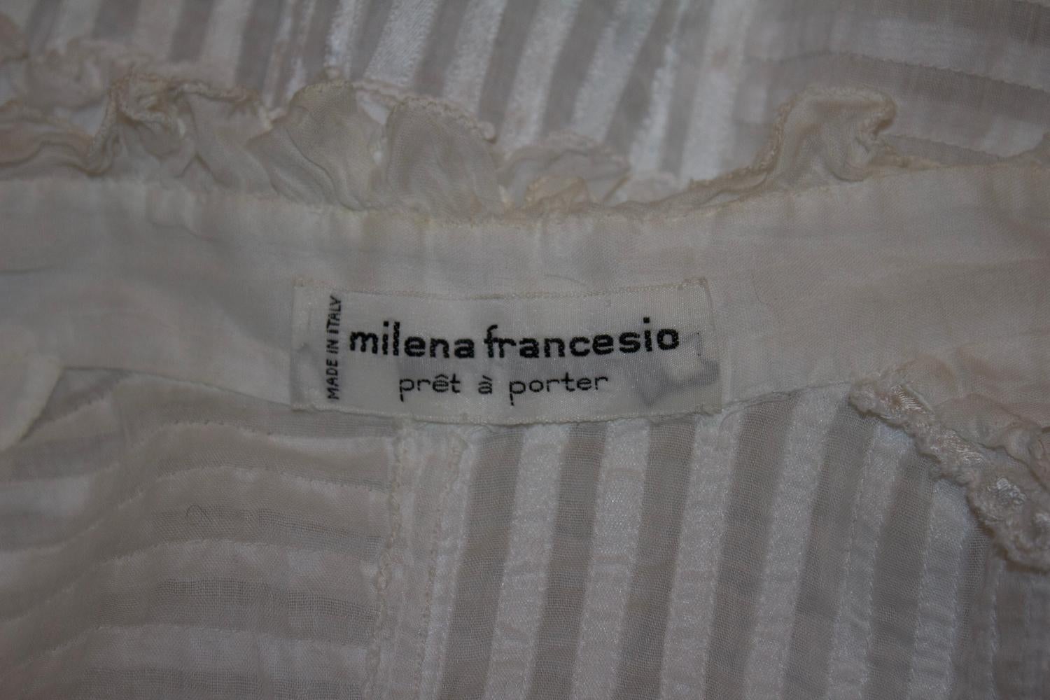 Una splendida camicetta vintage di Milena Francesio. Realizzata in Italia, la camicetta è in cotone con un meraviglioso nastro e un dettaglio di pieghe.  con dettagli a balze e polsini con lacci a nastro. 
Misure: Busto 36'', lunghezza 23''.