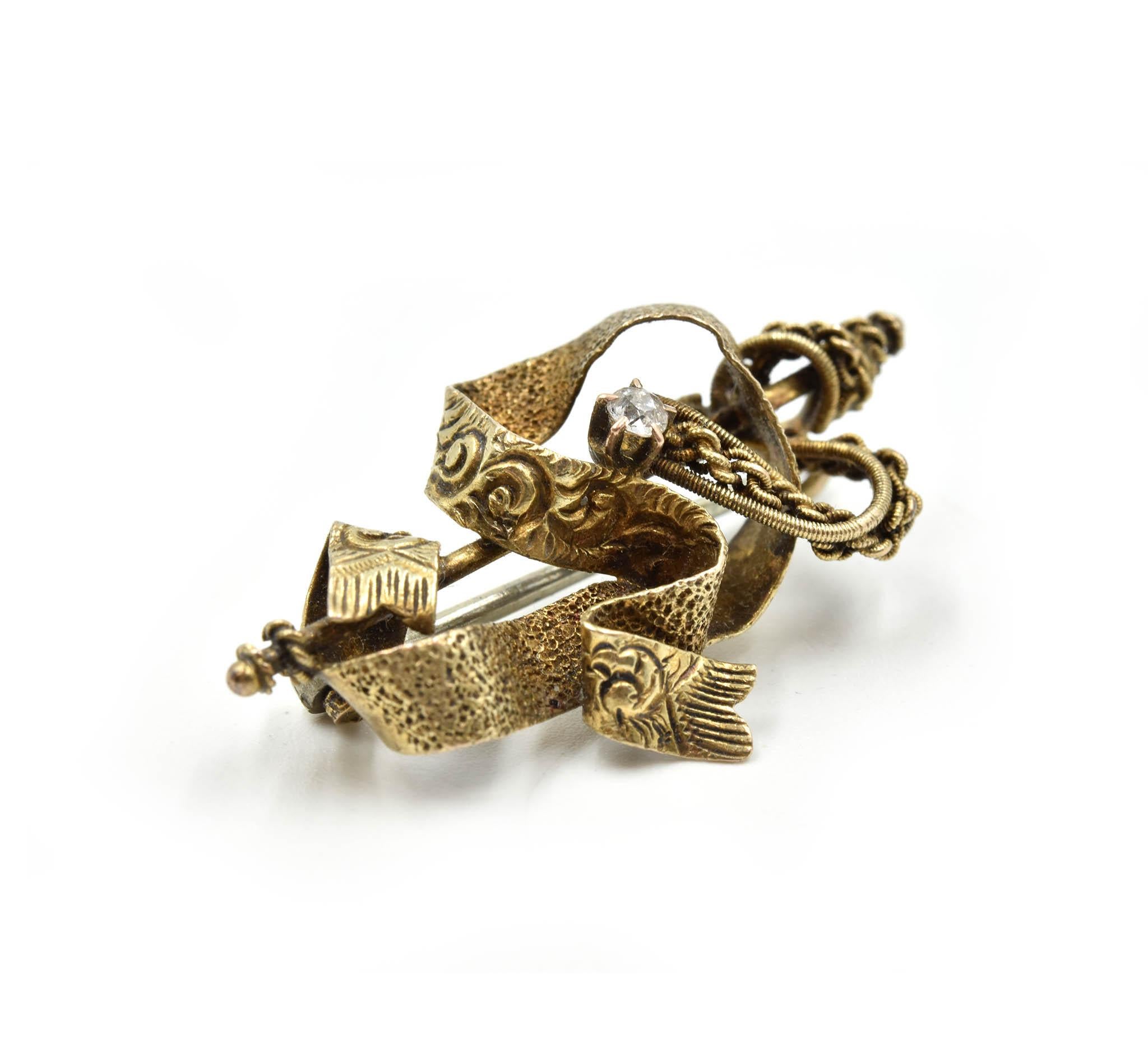 Designer: design personalizzato
Materiale: Oro giallo 10k
Diamante: un diamante tondo brillante di 0,06 carati di peso totale
Dimensioni: la spilla a nastro è lunga 1 pollice e mezzo e larga 3/4 di pollice. 
Peso: 3.90 grammi
