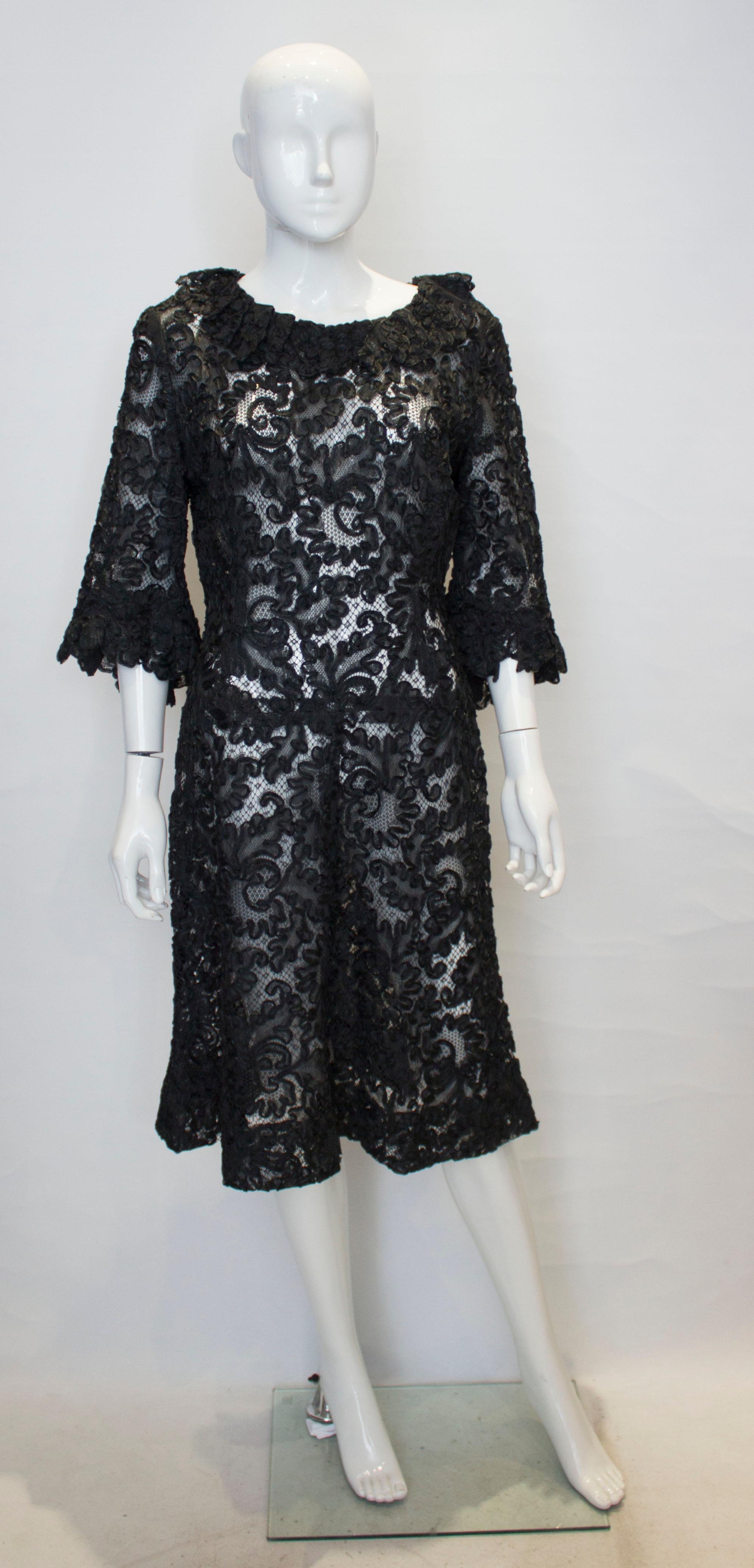 Ein schickes Cocktailkleid in schwarzer Schleifenoptik. Das Kleid hat Rüschendetails am Kragen und an den Manschetten sowie einen zentralen Reißverschluss am Rücken.
