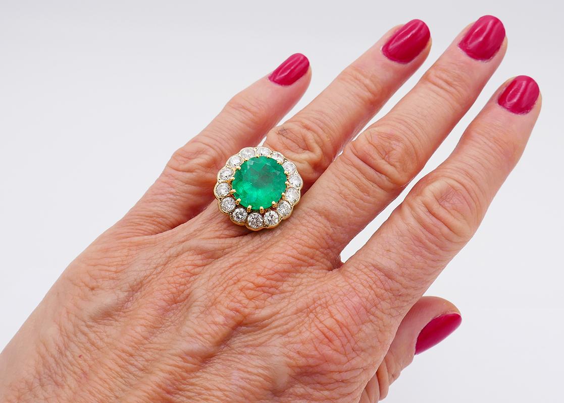          A classic cluster 18 karat yellow gold ring with a Colombian emerald and diamond. The emerald comes with a GRS Gemstone Report. 
	This gorgeous gold ring features a faceted oval emerald surrounded by a halo of fourteen bezel set diamonds