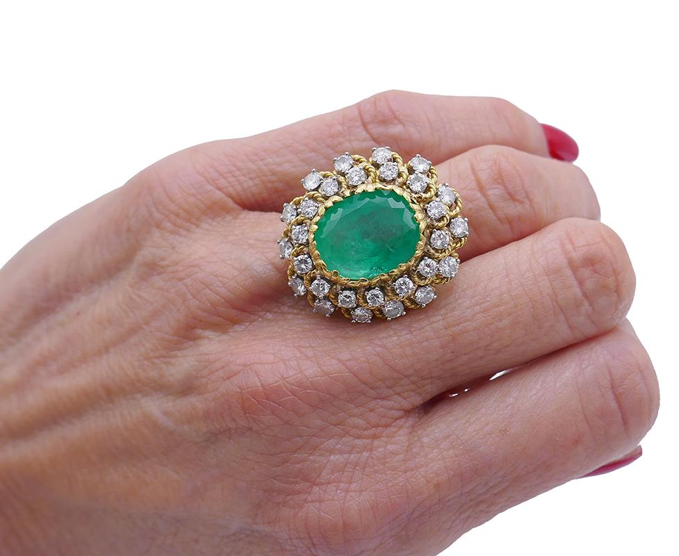          A massive oval faceted emerald round brilliant cut diamond ring made of 18k yellow gold. It’s an impressive Mid-century piece that carries a lot of character.  
	Two rows of diamonds surrounding the emerald are set one above another. The