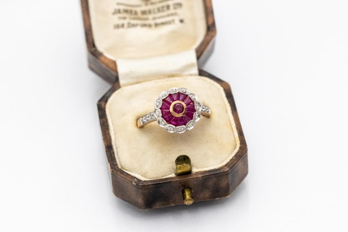 Blumenförmiger Vintage-Ring mit Rubinen und Diamanten.

Herkunft: Westeuropa, Mitte des 20. Jahrhunderts

Ein Ring in Form einer Blume, besetzt mit natürlichen Rubinen von 1,00 ct und verziert mit einem Halo aus 18 Diamanten im Brillantschliff von