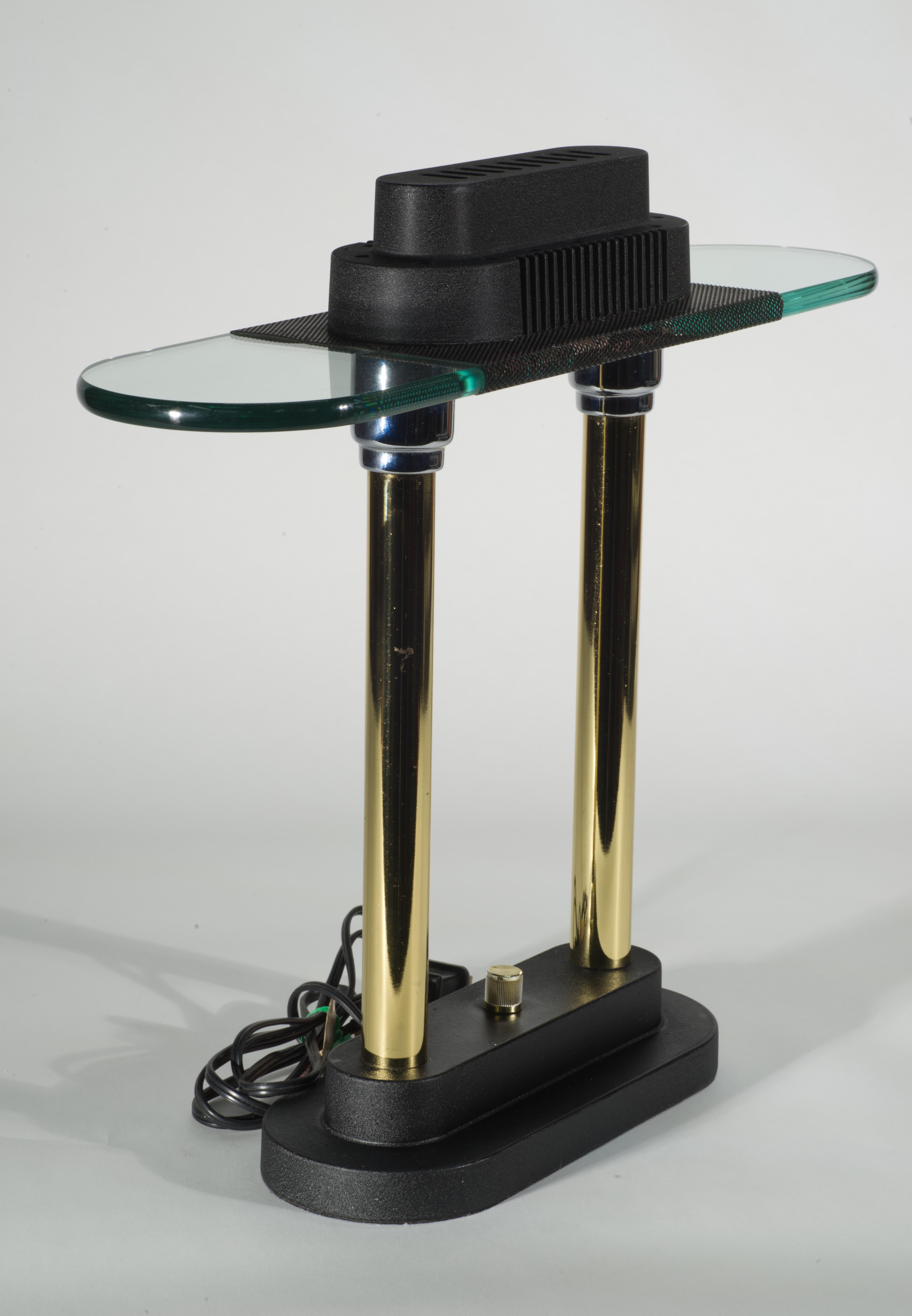  Vintage table lamp features sculptural shape with stepped black base and top structures; the top structure ends with an undermounted glass disk, discreetly supported by two metal columns, that seems to float, reminiscent of a flying saucer.