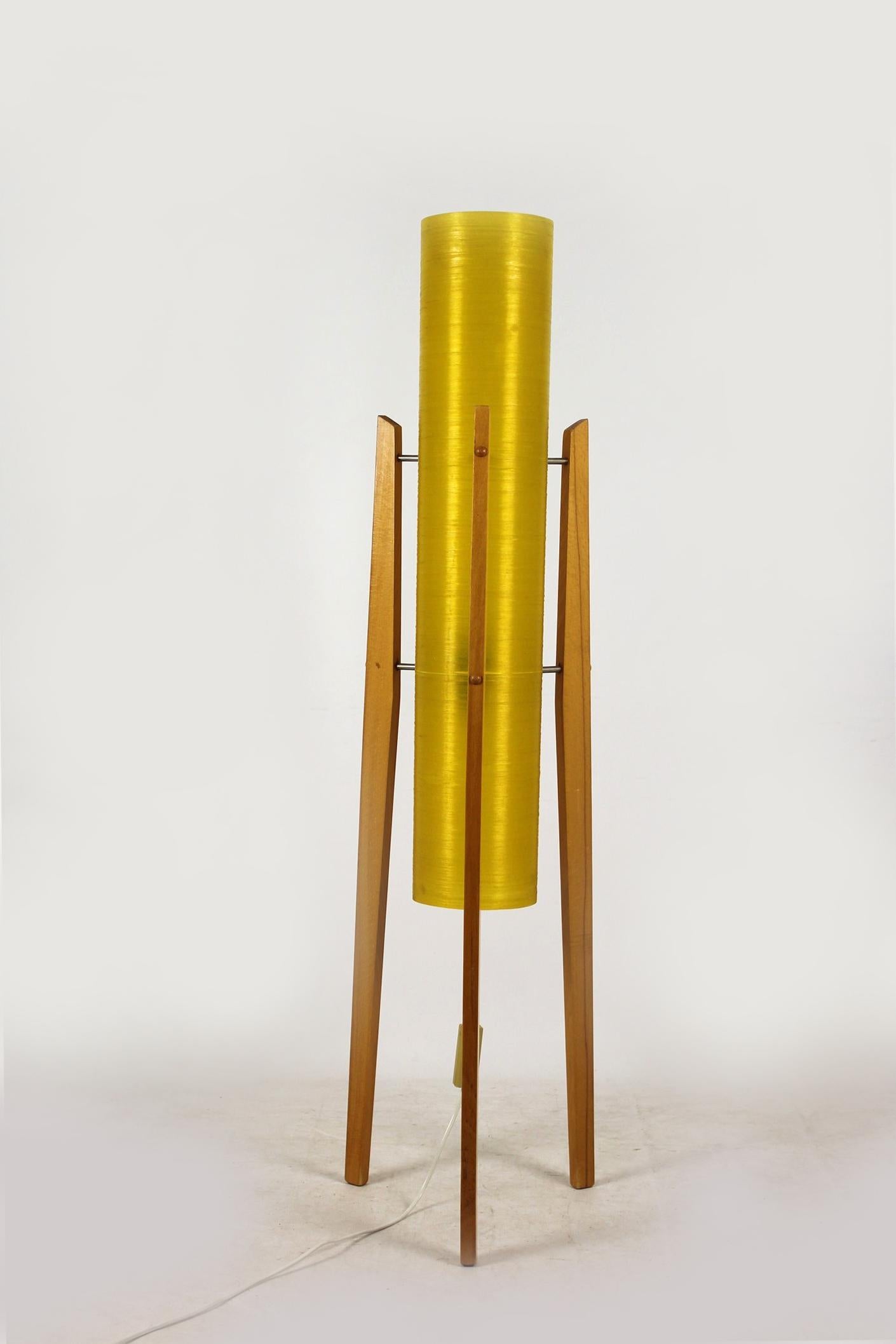 This rocket floor lamp was produced in the 1960s in Czechoslovakia. It features a yellow fiberglass shade on three wooden legs. The lamp is fully functional and requires one bulb.