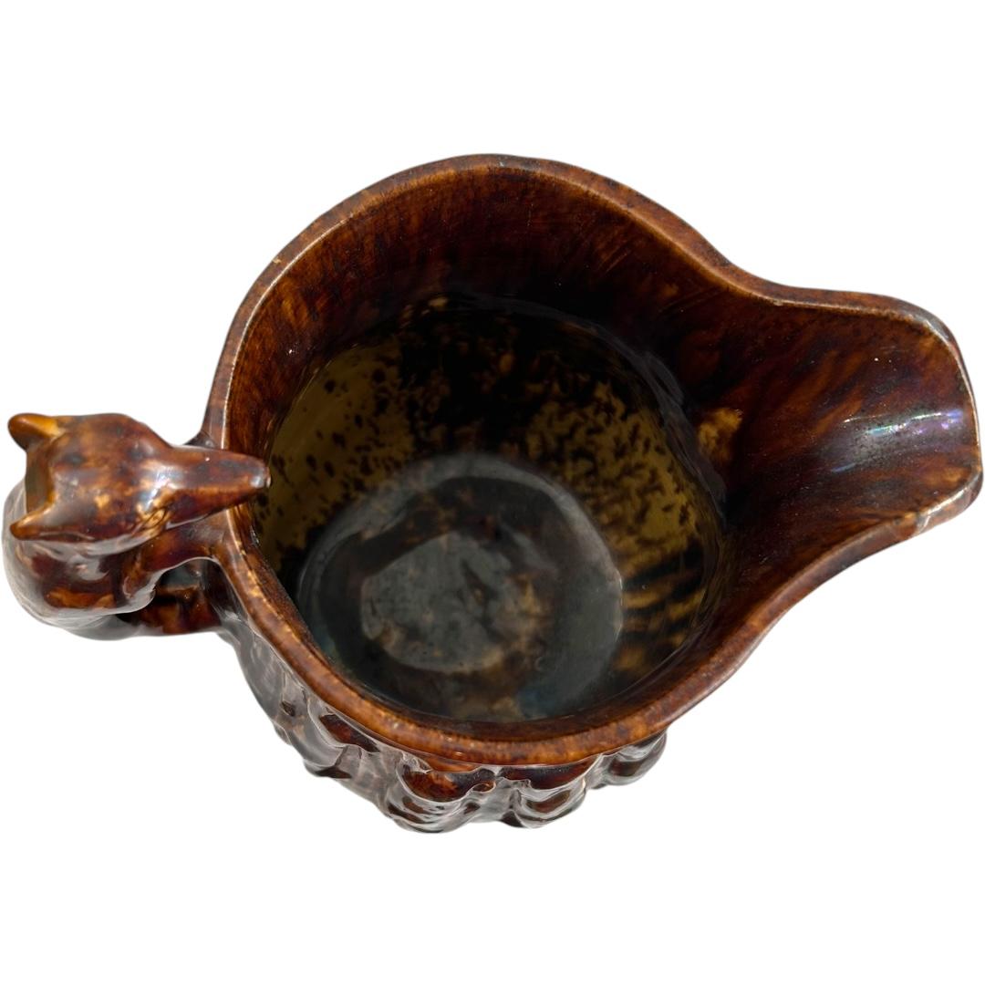 This vintage Rockingham clay molded pitcher with a hound handle is a great addition to your collection.  The pitcher features a unique hunt scene design that is sure to catch the eye of any collector.  The surface is covered in a reddish-brown