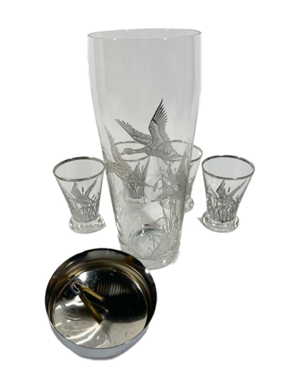 Mid-Century modern cocktail shaker and 4 cocktail glasses in clear glass with a silver overlaid design of three ducks in flight among cattails and the shaker with chrome lid.