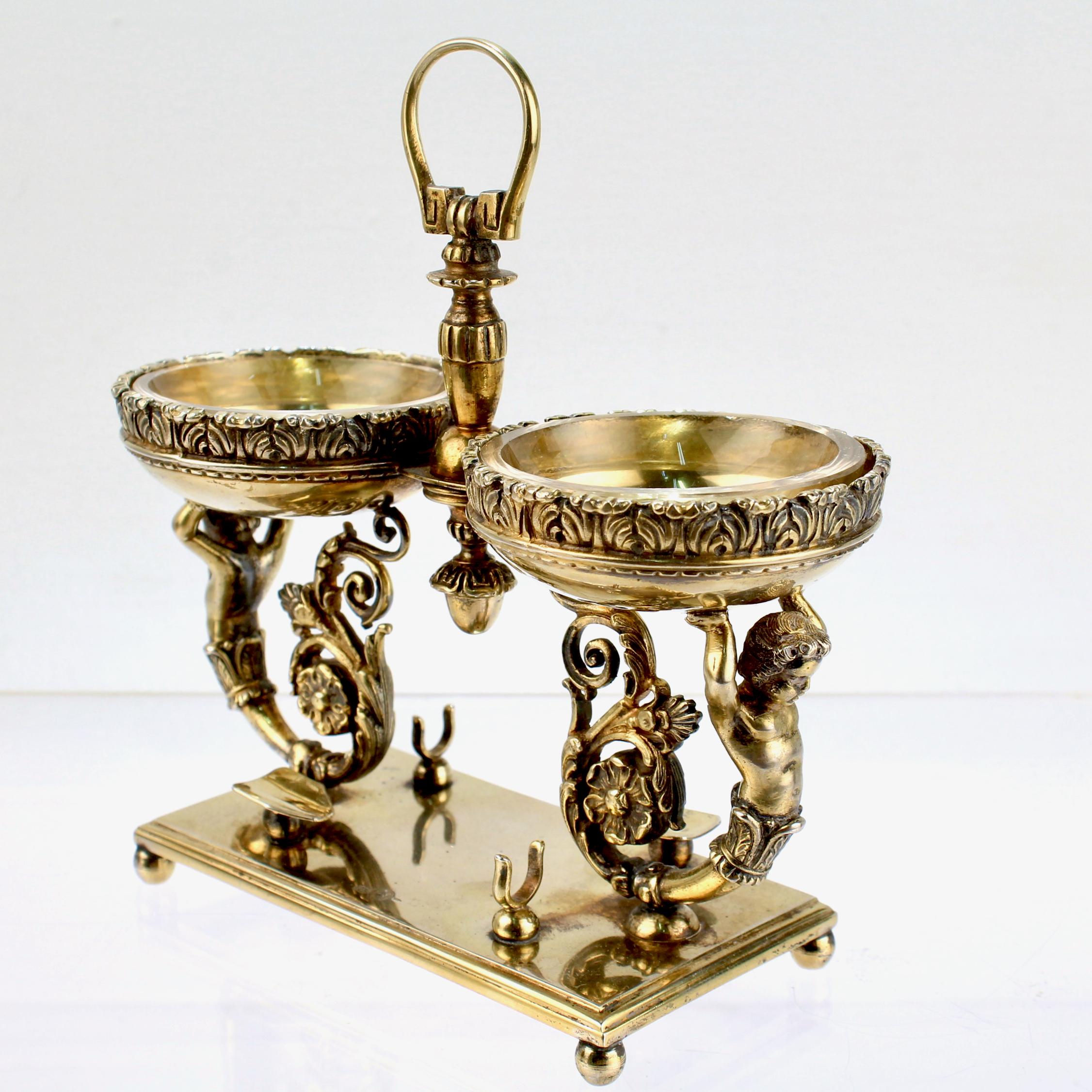 A fine Italian double caviar stand or holder.

In 800 silver with a gold wash.

Having figural half-cherub supports on a flat plinth with two spoon rests and ornate chased decoration throughout.

Together with its 2 original glass liners.

Simply a
