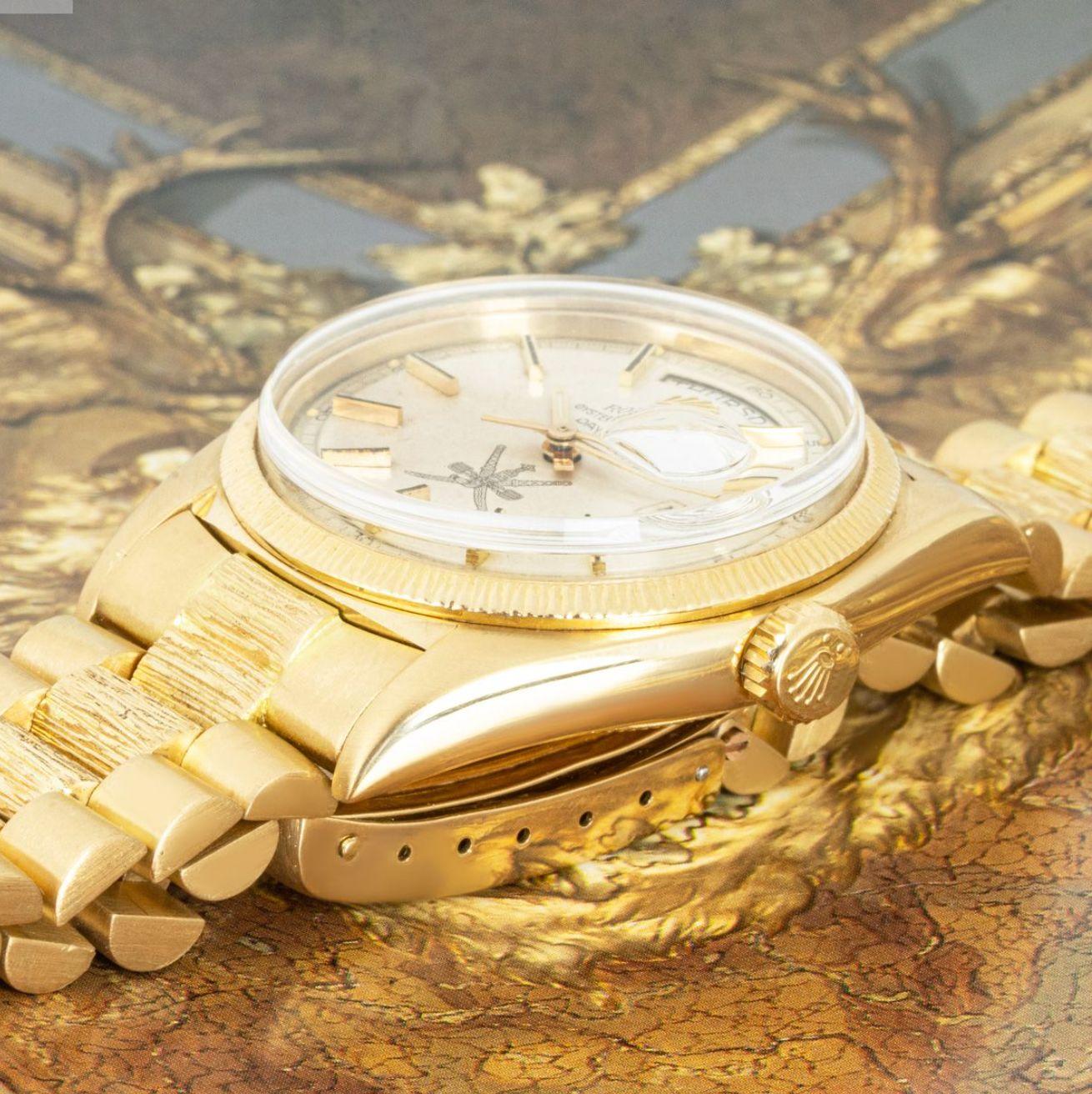 Montre-bracelet Day-Date en or jaune 18 carats de Rolex. Cadran argenté avec index appliqués, écusson omanais à 6 heures, représentant l'emblème national d'Oman, et lunette en or jaune.

Dotée d'un verre en plastique, d'un mouvement automatique à