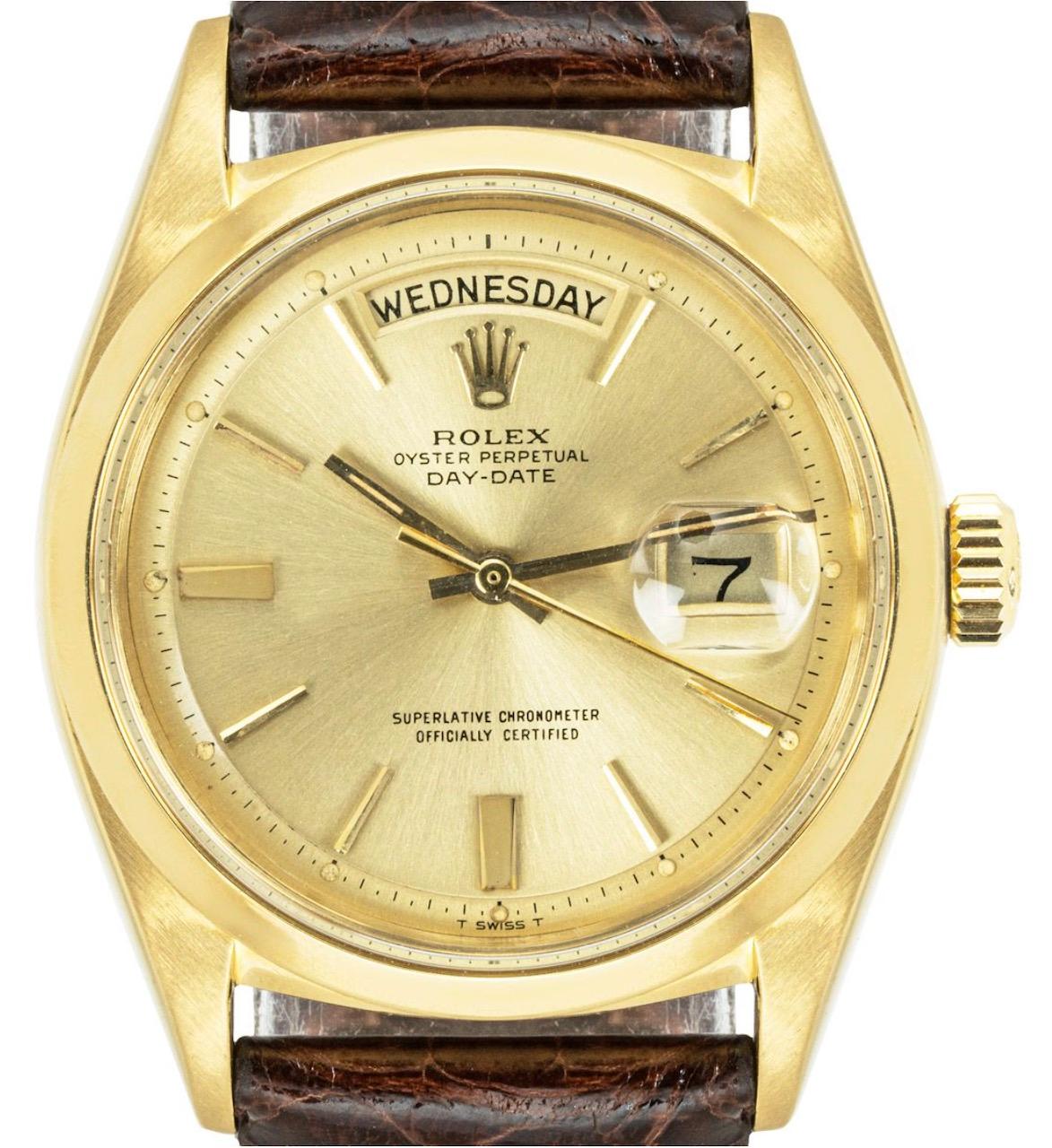 A vintage yellow gold Day-Date wristwatch. Features a champagne dial with applied hour markers and a smooth fixed bezel. Fitted with plastic glass, a self-winding automatic movement and a brown generic leather strap equipped with a gold plated pin