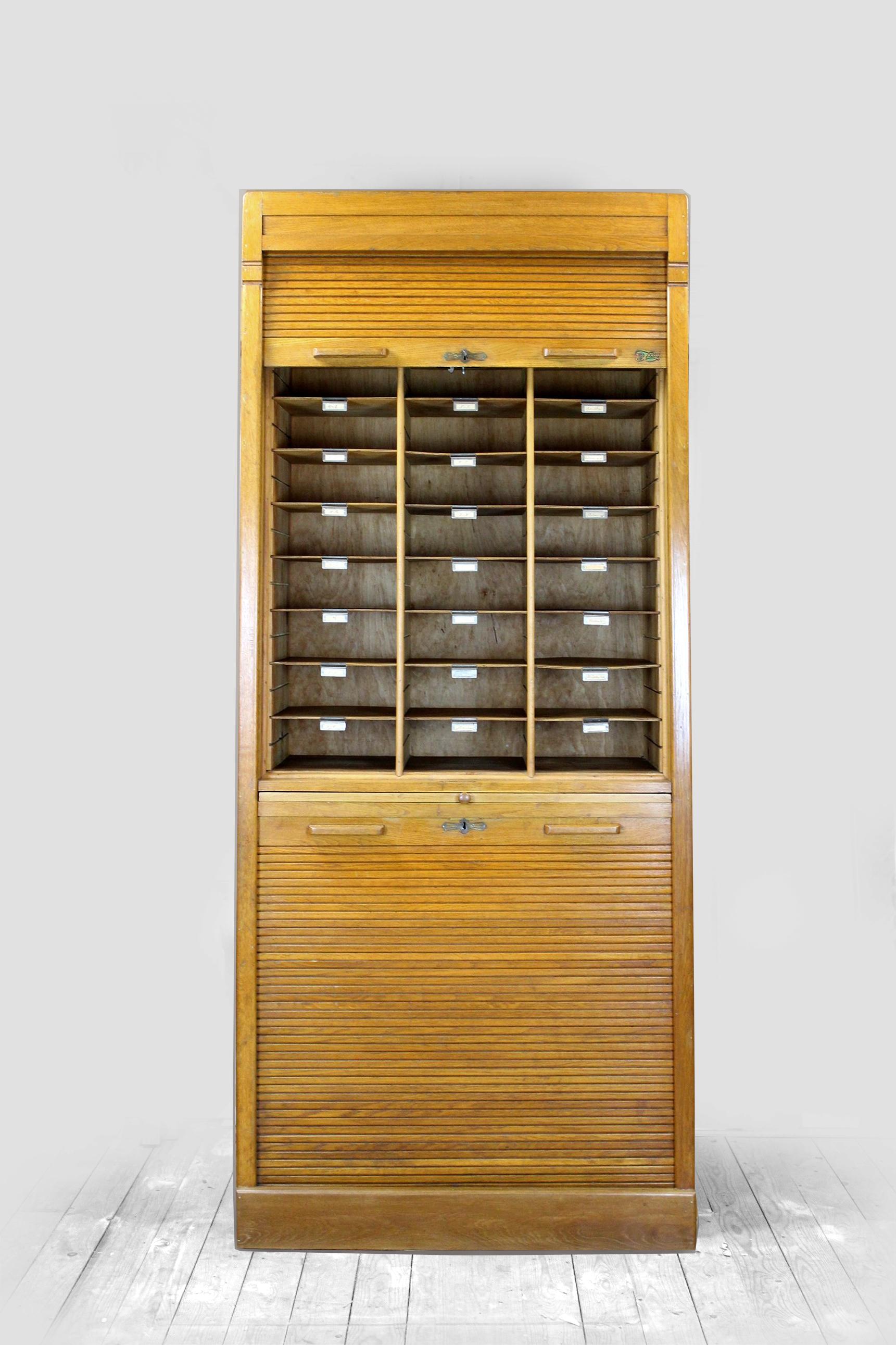 This oak filing cabinet was produced in the 1930s in the USA by the Jerry company. 
The cabinet has two roller shutters and a sliding shelf in the middle. 
The shutters work easily, they are locked with a key (one key included, fits both locks).