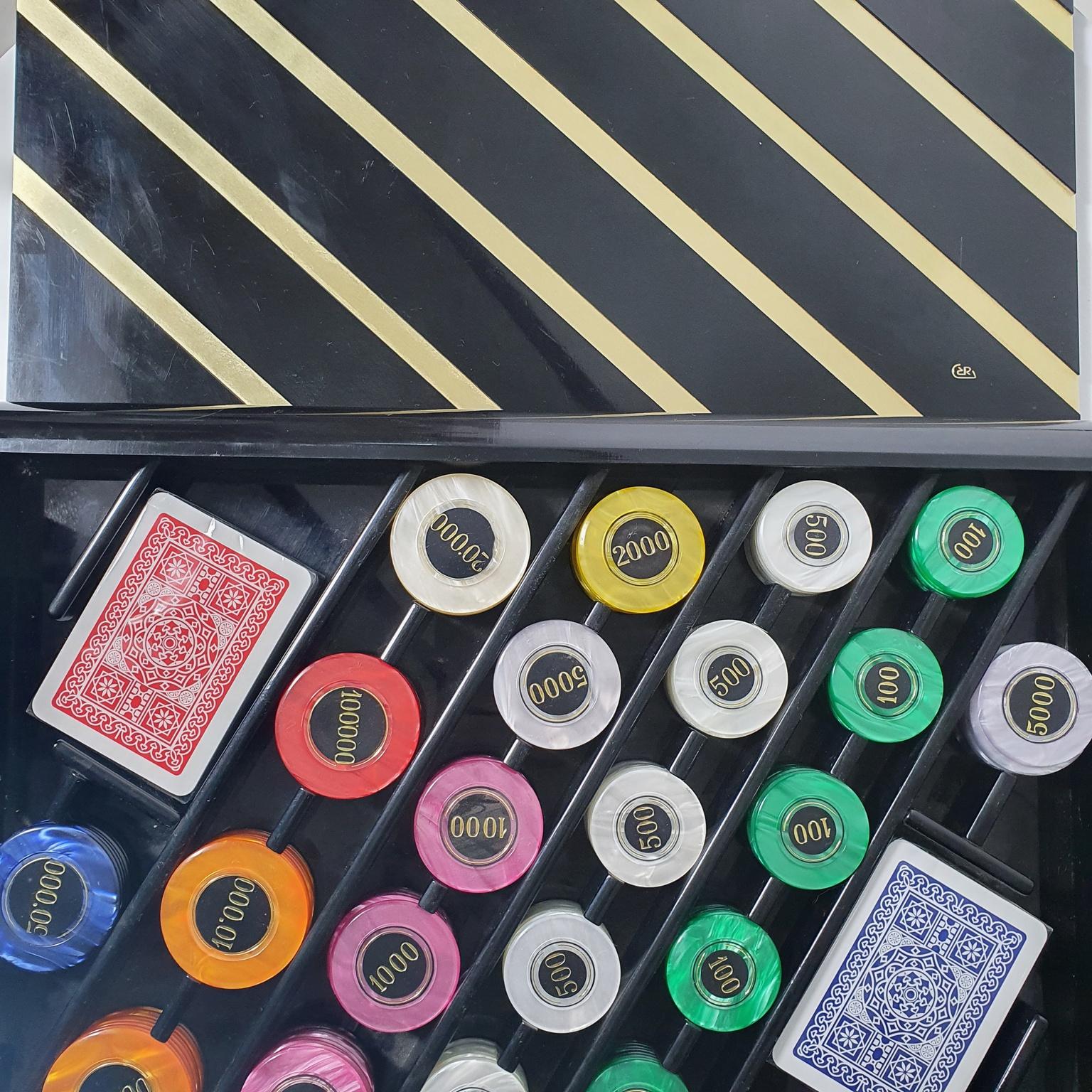 This is a rare vintage Romeo Rega Poker set with RR mirrored logo on top of the lid. The box of the poker set is made in black plexiglass decorated with diagonal metal strips on the lid.
This poker set is in perfect condition with the decks of