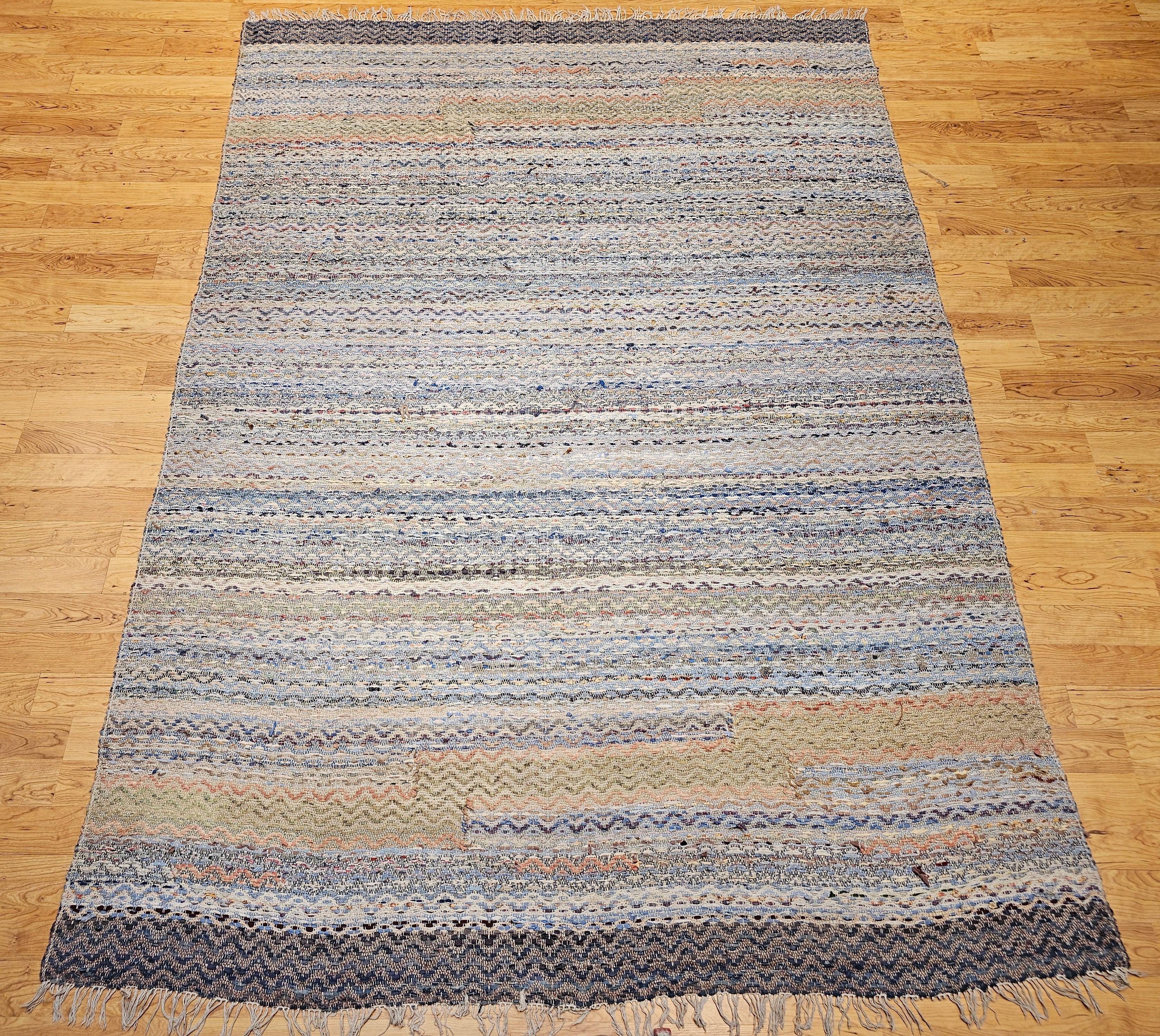 A charming and character-filled vintage American rag rug from the early 1900s, handwoven in a vibrant multicolor stripe pattern. This large room-size rug showcases a spectrum of soft and earthy hues—pale blue, green, ivory, yellow, brown, pink, red,