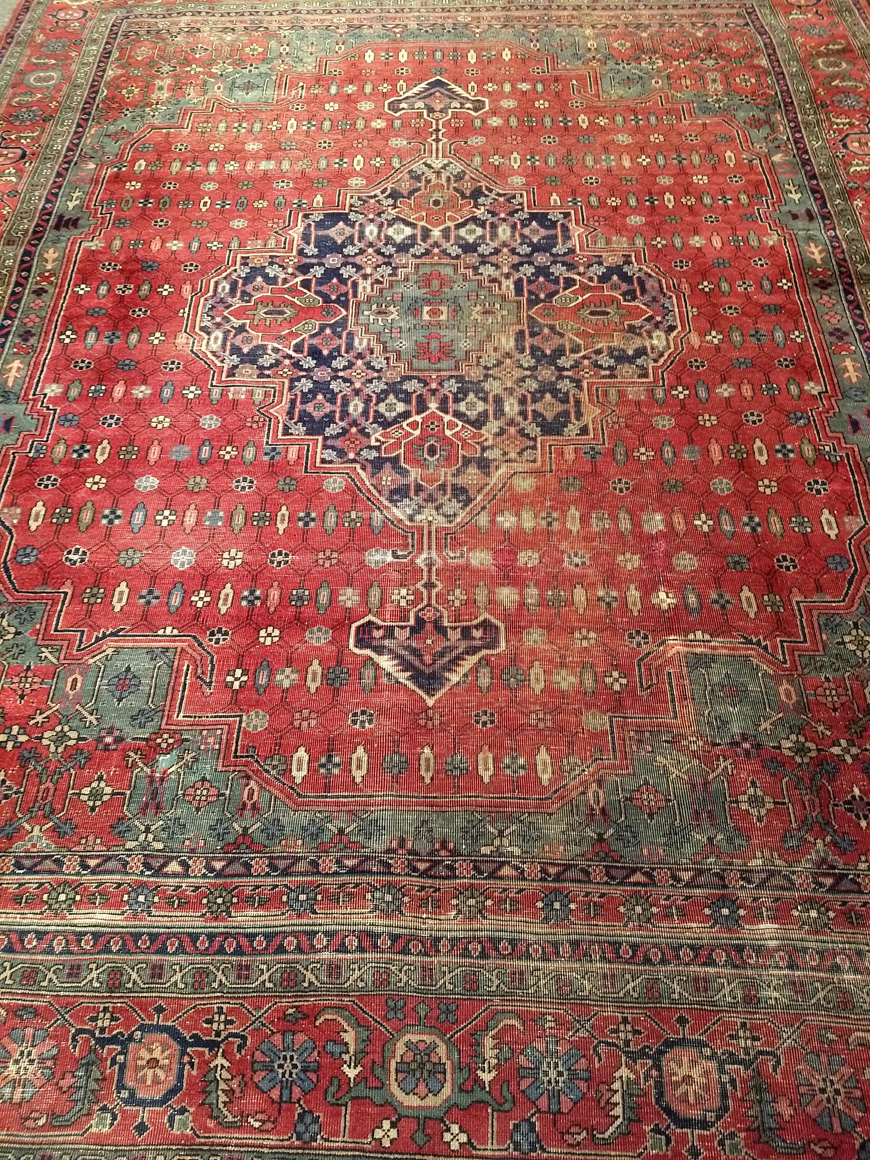 This striking vintage Turkish rug, hand-knotted in a classic Persian Heriz medallion pattern, offers a bold geometric aesthetic and a vibrant, well-balanced color palette. Featuring a large central medallion in navy blue, red, and green, the design