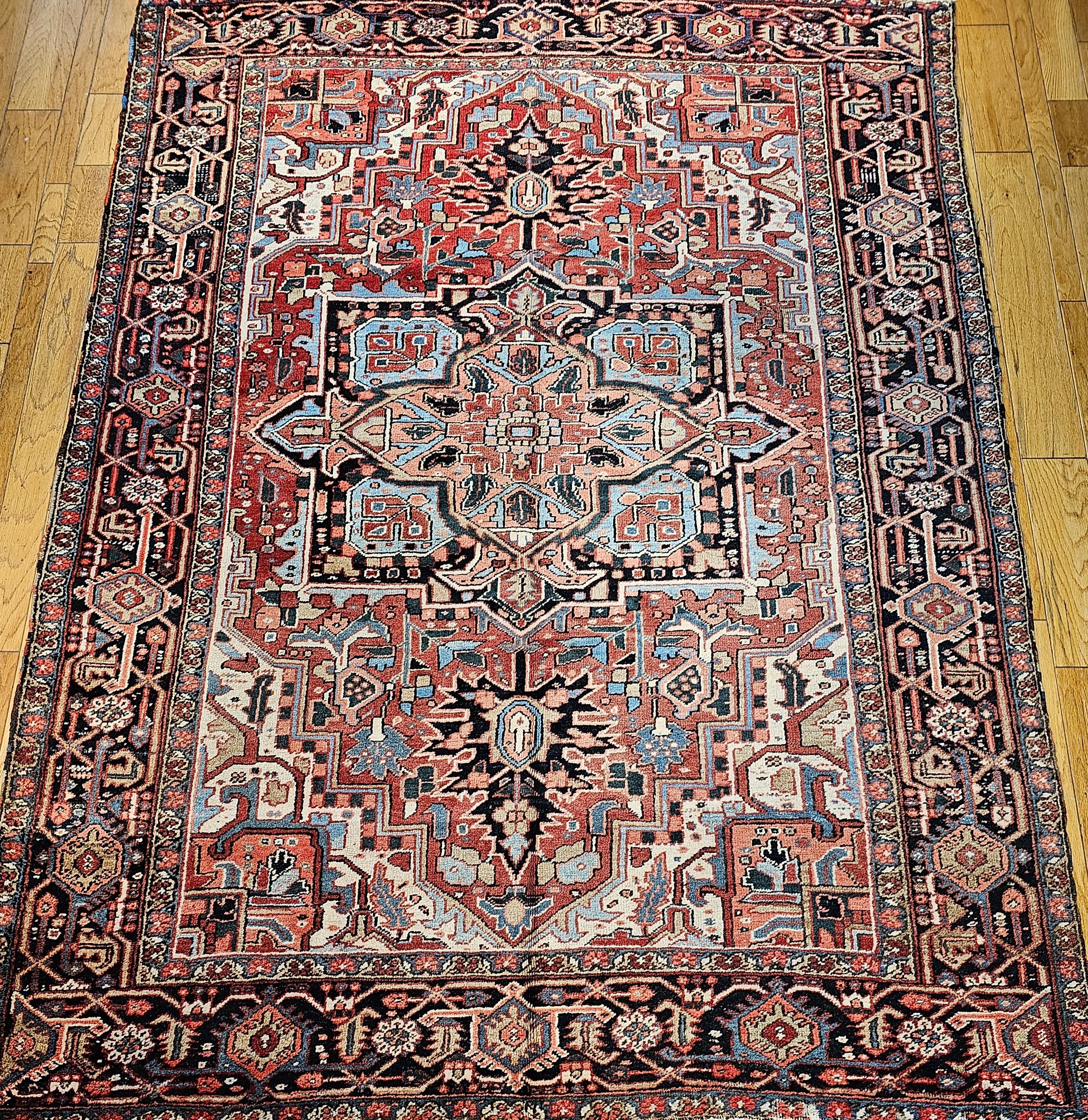 The antique room-size Heriz rug with Serapi design and colors from NW Persia from the early 20th century.  This Heriz has a brick red color field with wonderful “abrash” colors in green, light blue, pink, and yellow designs through the field and