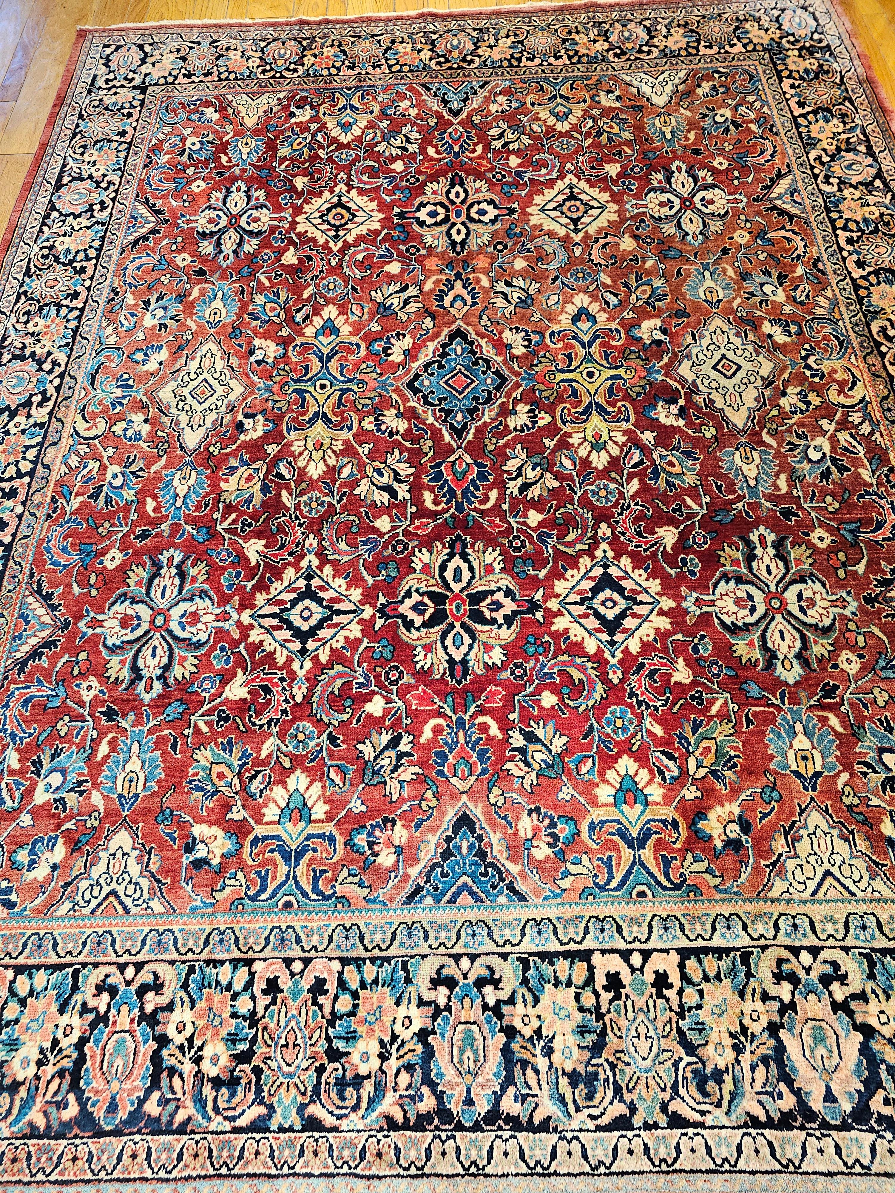 The vintage Persian Mahal Sultanabad room size rug with an allover design pattern of  large geometric forms interwoven with larger flower forms is in the red field and a dark navy blue border. The use of bright reds, blue, pink, and shades of other