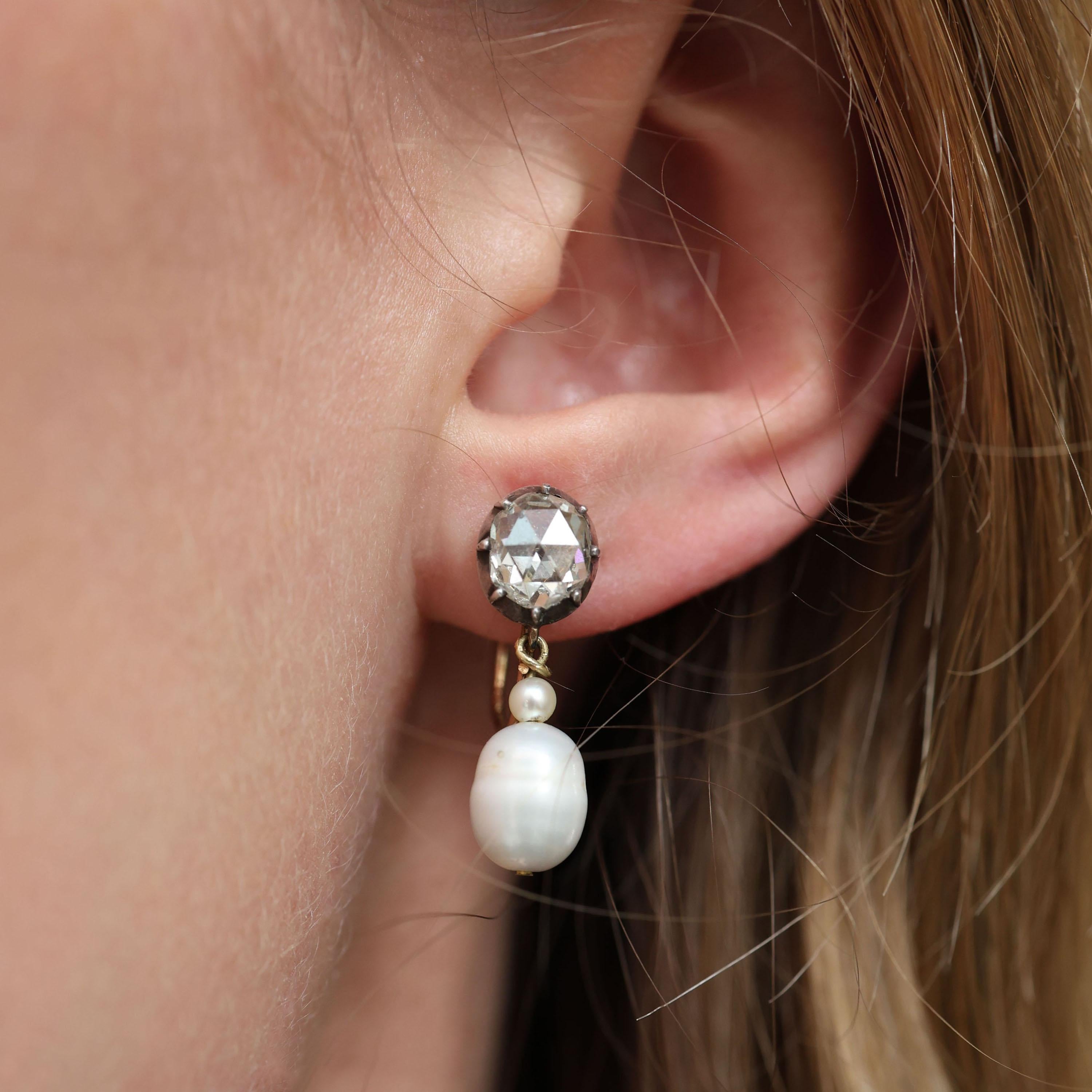 A pair of vintage rose-cut diamond and pearl drop earrings, each with a single rose-cut diamond, in a silver cut down setting, upon a scallop pierced gold gallery, with pendant drops, with an oval baroque pearl and a small round pearl above, on gold