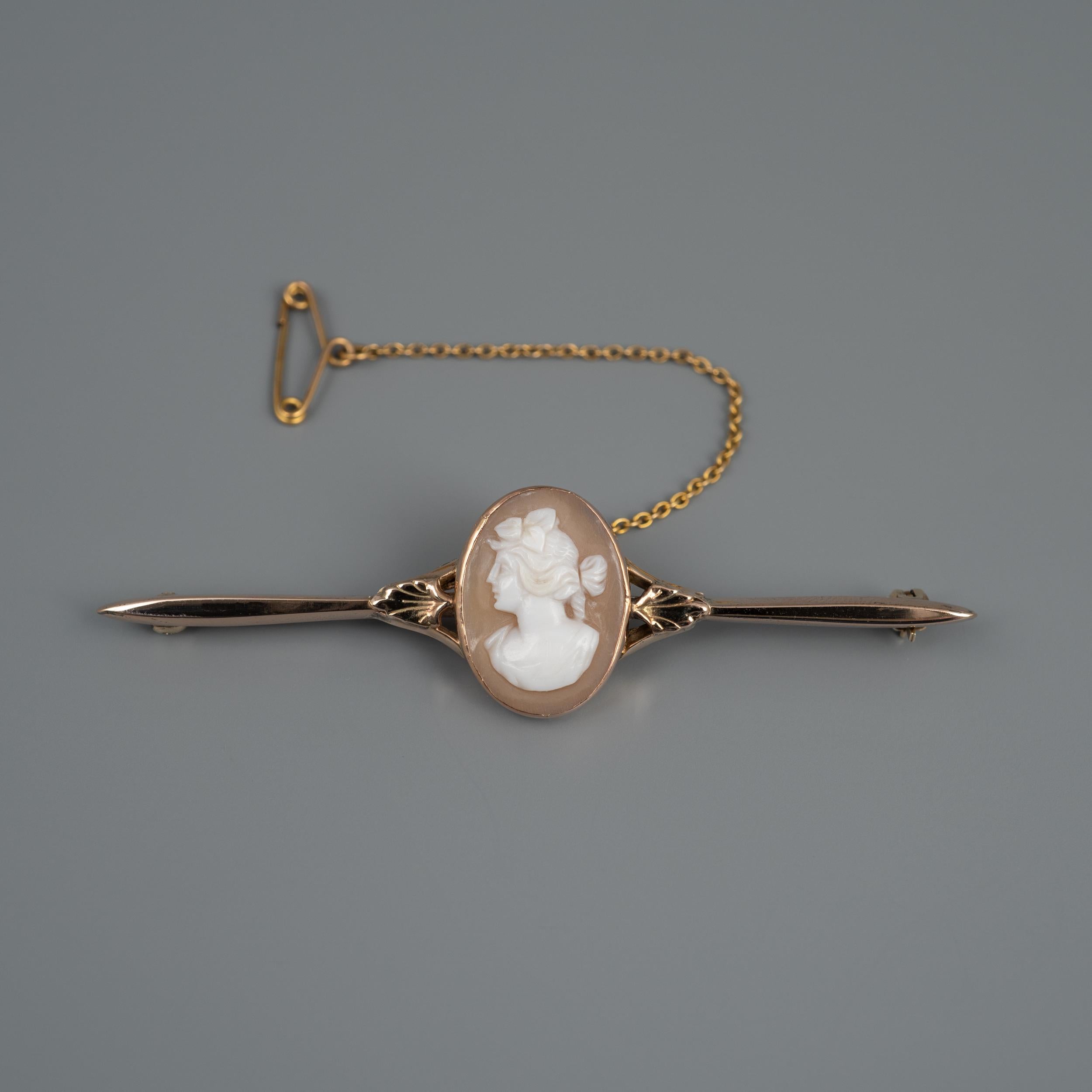 This vintage rose gold bar brooch features a center oval cameo with female portrait carved from sardonyx shell and set in an oval mount which has fantastic gold leaf detail on either side. The bar has an elegant graduated elongated eclipse shape