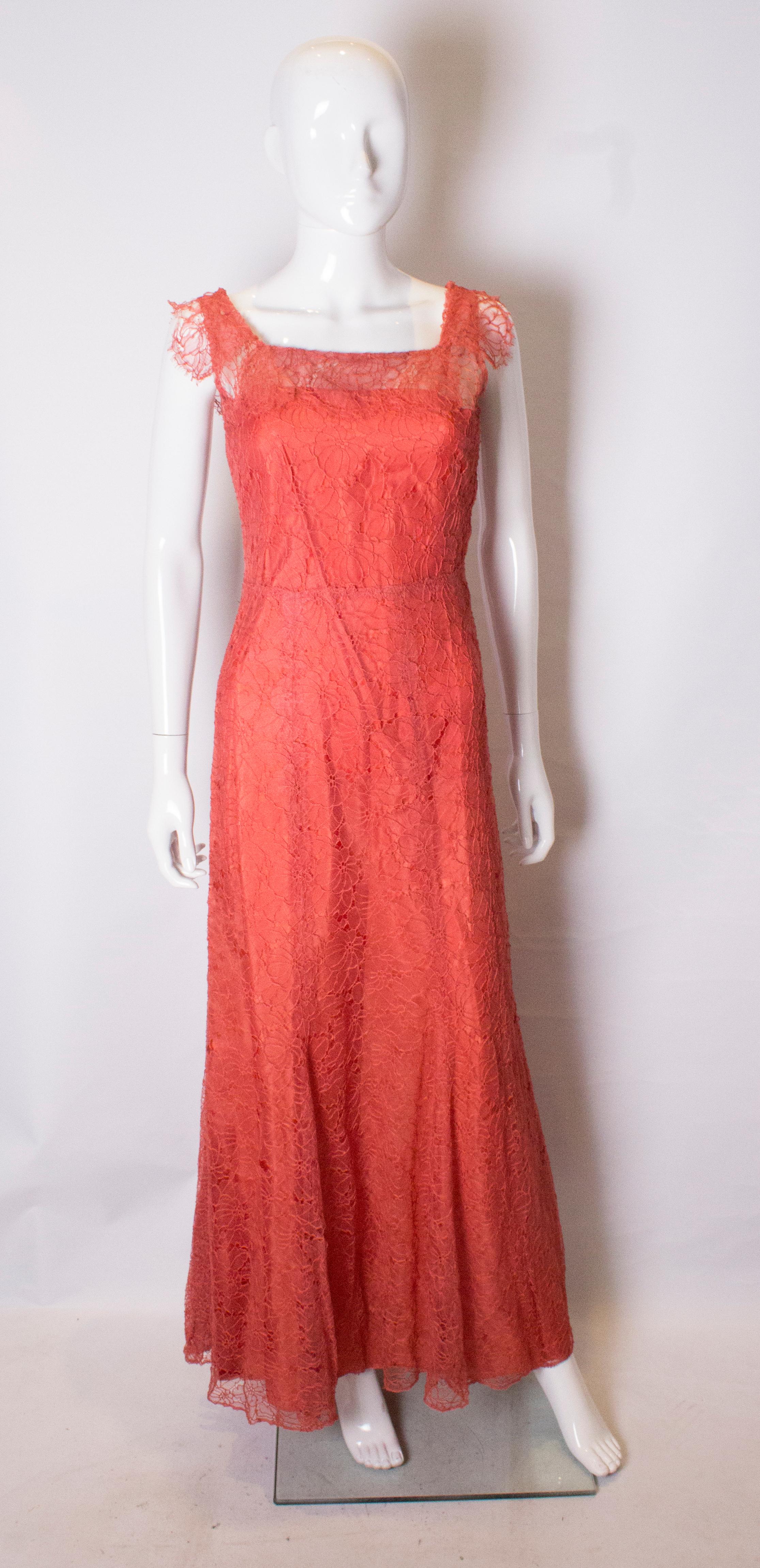 A stunning rose pink lace gown from the 1930s. The dress has a v back line, side opening with hooks and eyes , and a drape over the front and arm holes. The dress comes with a  full length slip.