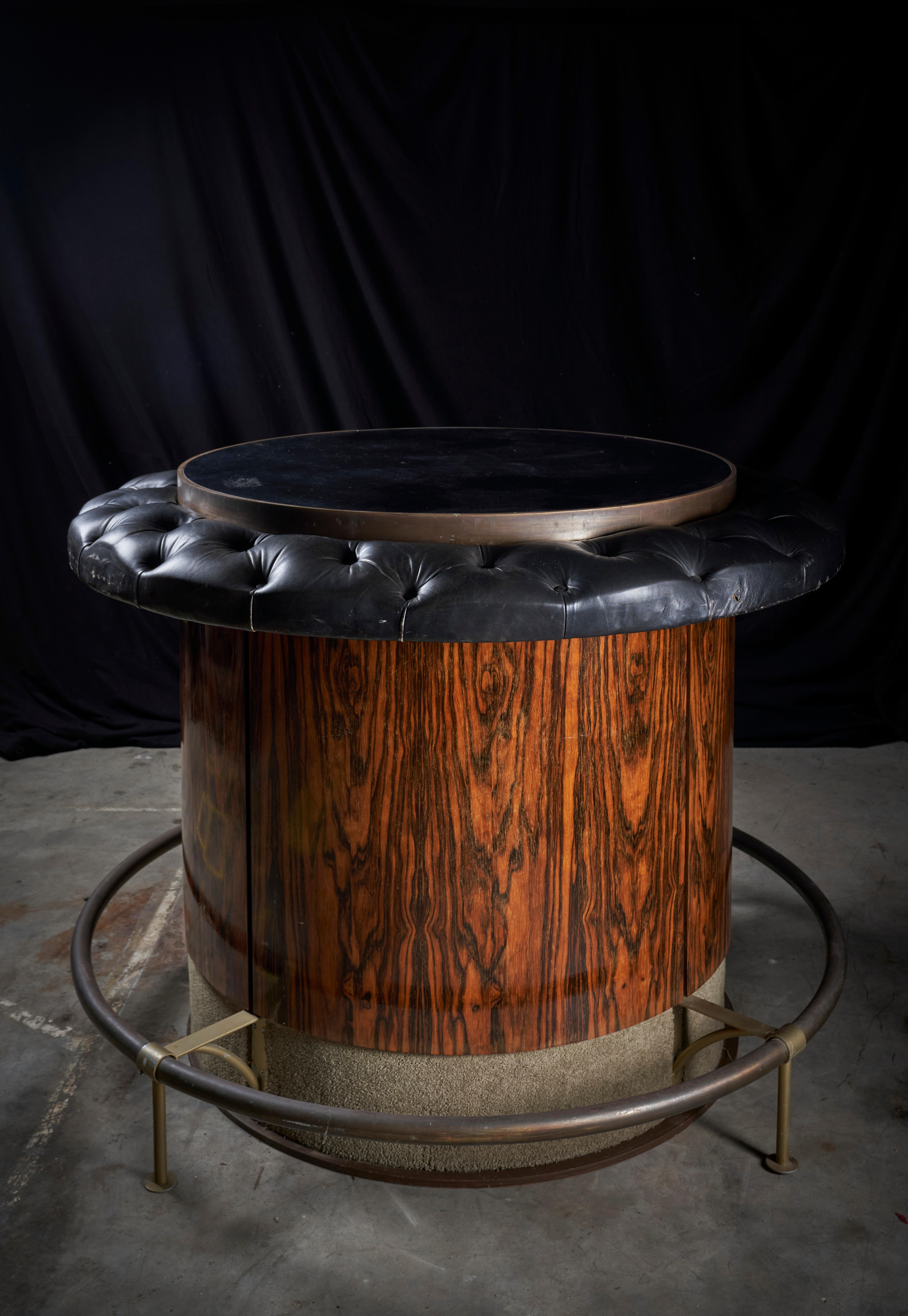 Esta llamativa mesa de bar vintage es una mezcla perfecta de elegancia y funcionalidad. Fabricado en rico palisandro, presenta un diseño circular que destila sofisticación de mediados de siglo. El tablero de la mesa está envuelto en lujoso cuero