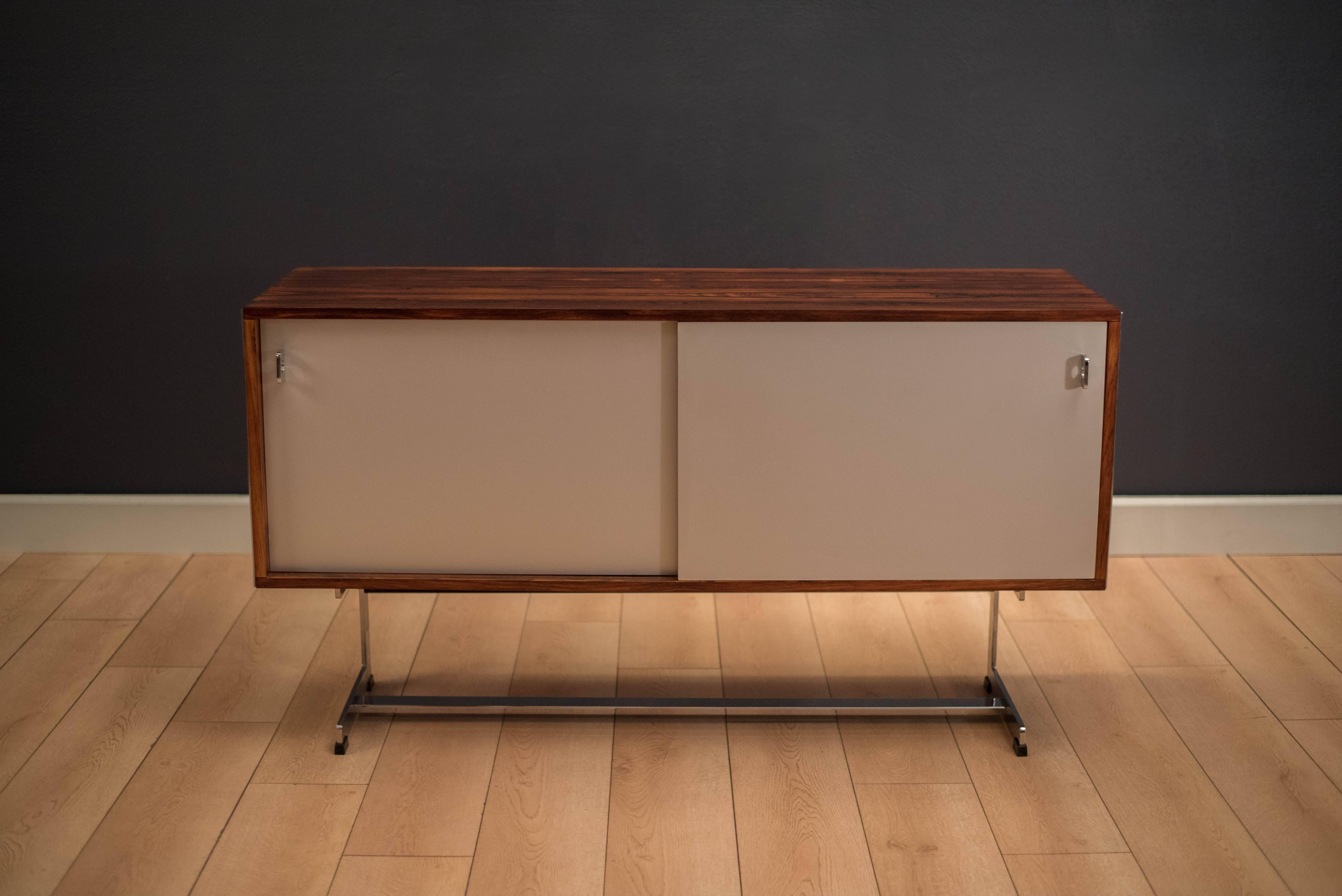 Mid-Century Modern credenza by Richard Young for Merrow Associates in rosewood. This piece features sliding aluminum doors with chrome side panels, pulls, and base. Interior cabinet includes open storage space with two adjustable glass shelves. This
