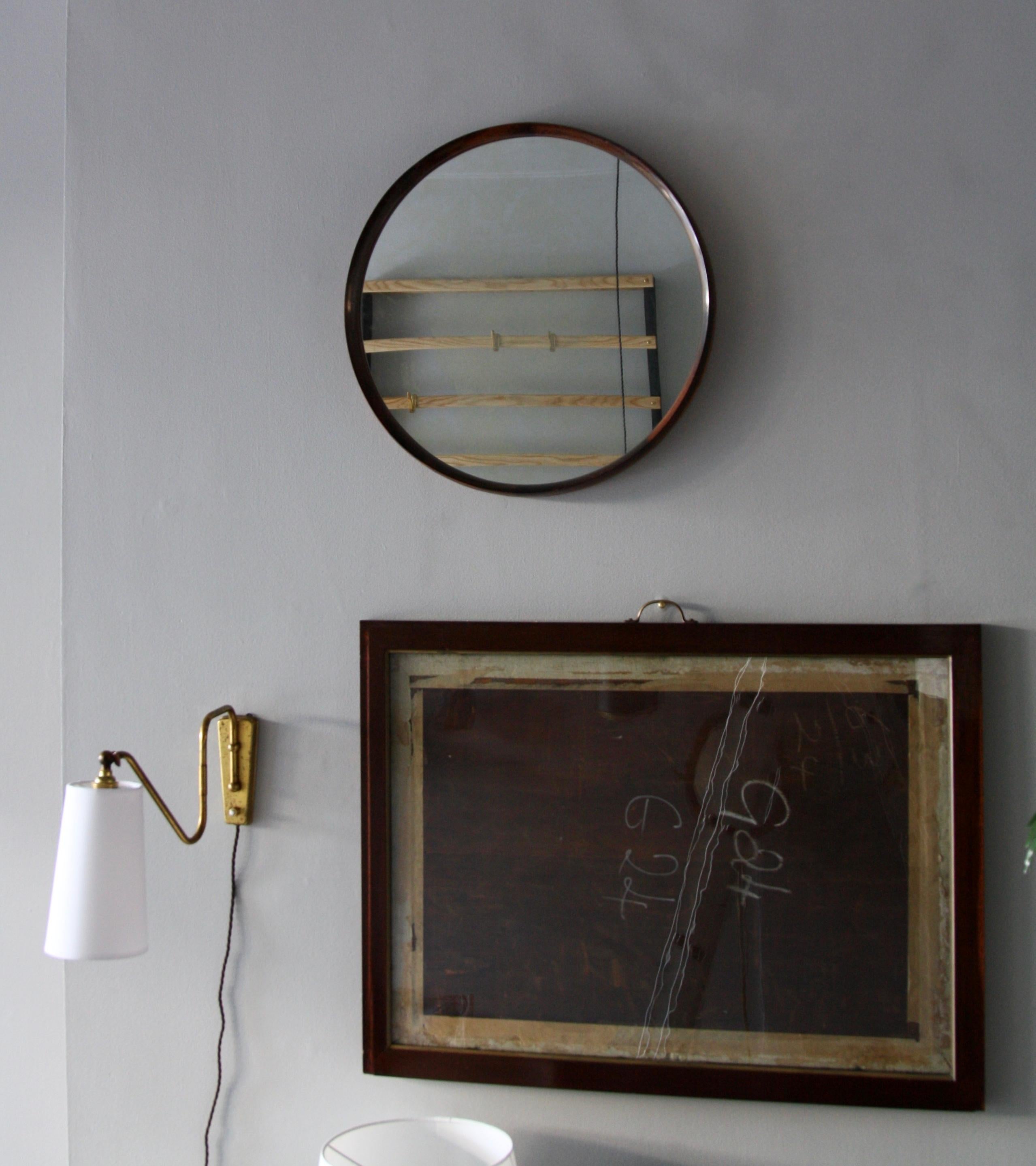 A large round vintage wall mirror made in Denmark, circa 1950. The mirror is made of sections of solid rosewood which are joined together using finger joints. A tan leather inlay bands the outer circumference of the mirror. The exposed construction,