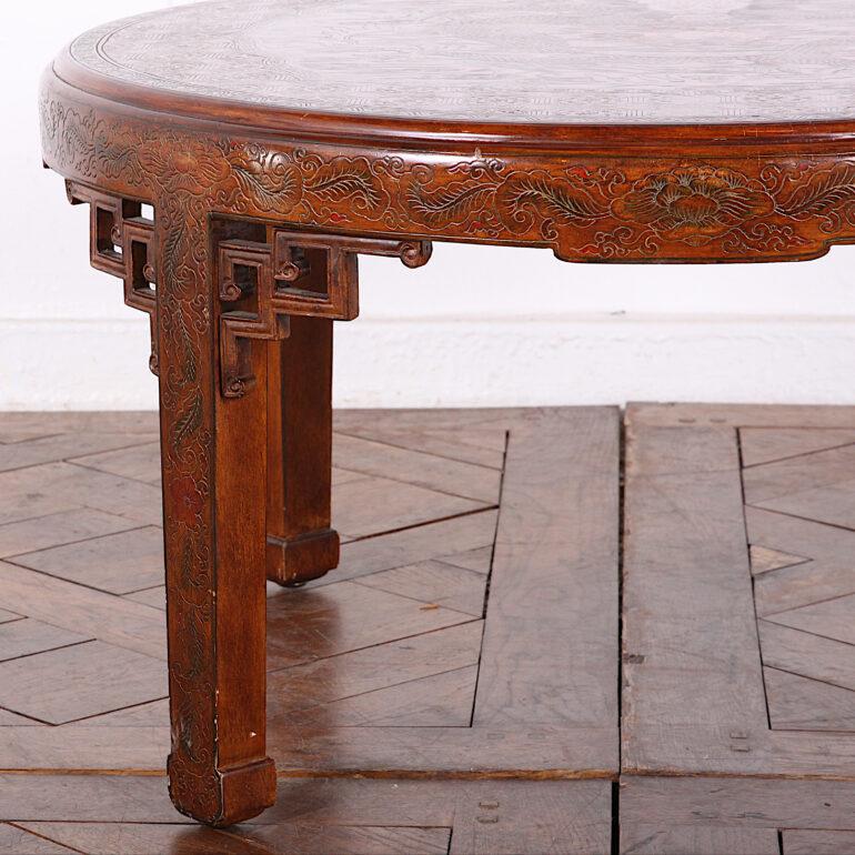 A mid-20th century Chinese round lacquer coffee table, the top featuring an incised and painted dragon surrounded by clouds within a detailed geometric border, the whole raised on simple square-profile legs with pierce-carved Ming-style corner