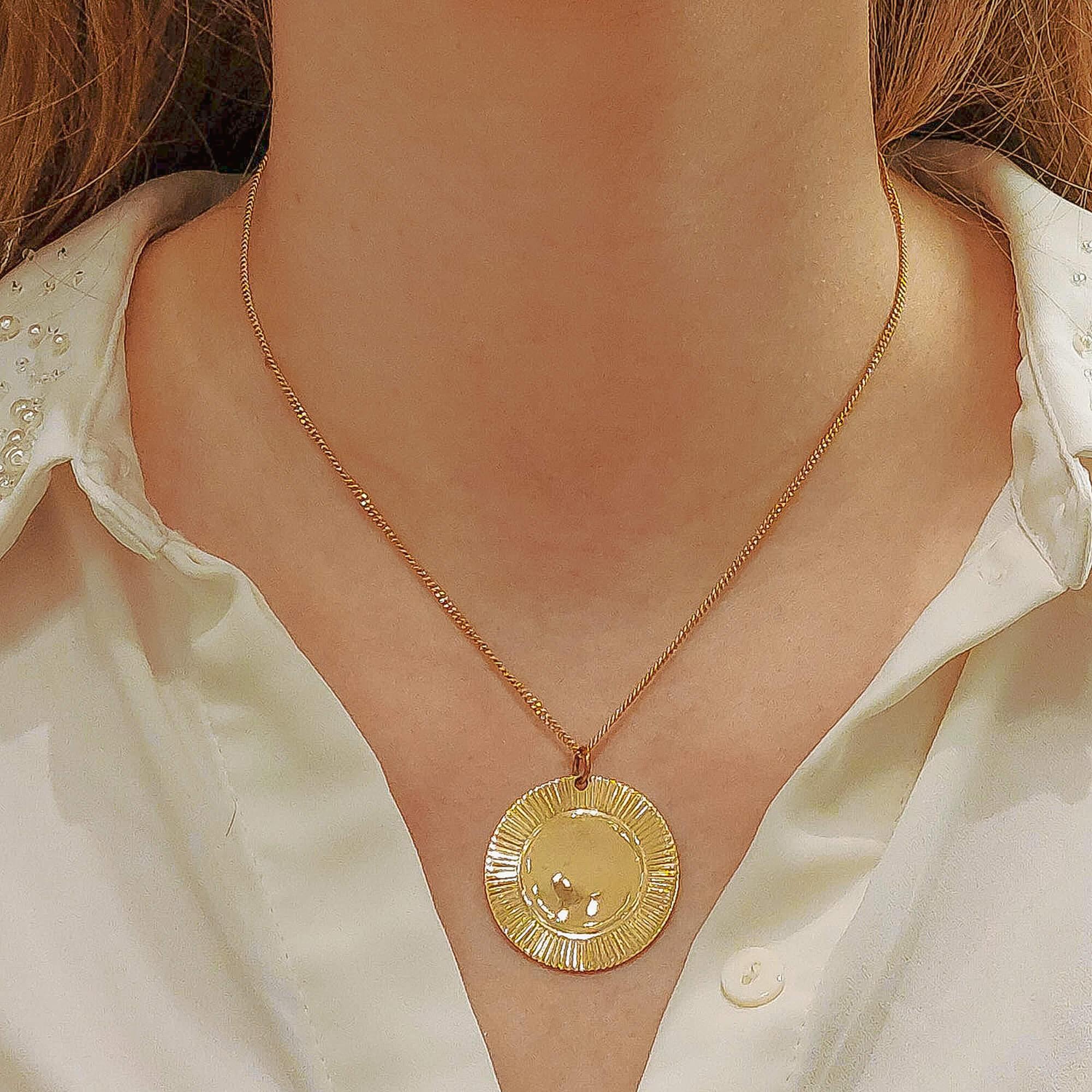 A simple coin/disc pendant made of solid 9k yellow gold. The disc has a lovely ‘crimple’ design around the edge, almost resembling a sun. The back and center have been left bare so that the wearer has to option to customize the disc with engraving