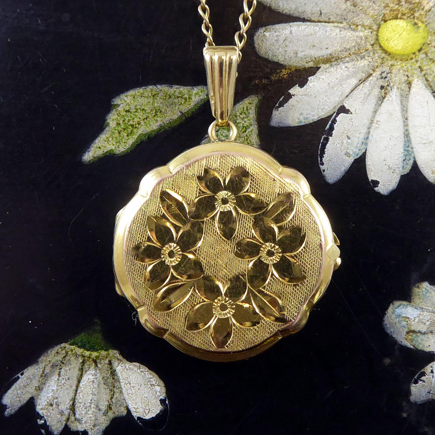 A vintage gold locket from the late 1980s being an overall round shape with scalloped edge.  The locket is engraved to the front half with floral garland in polished gold against a textured background.  The reverse of the locket is plain and bears