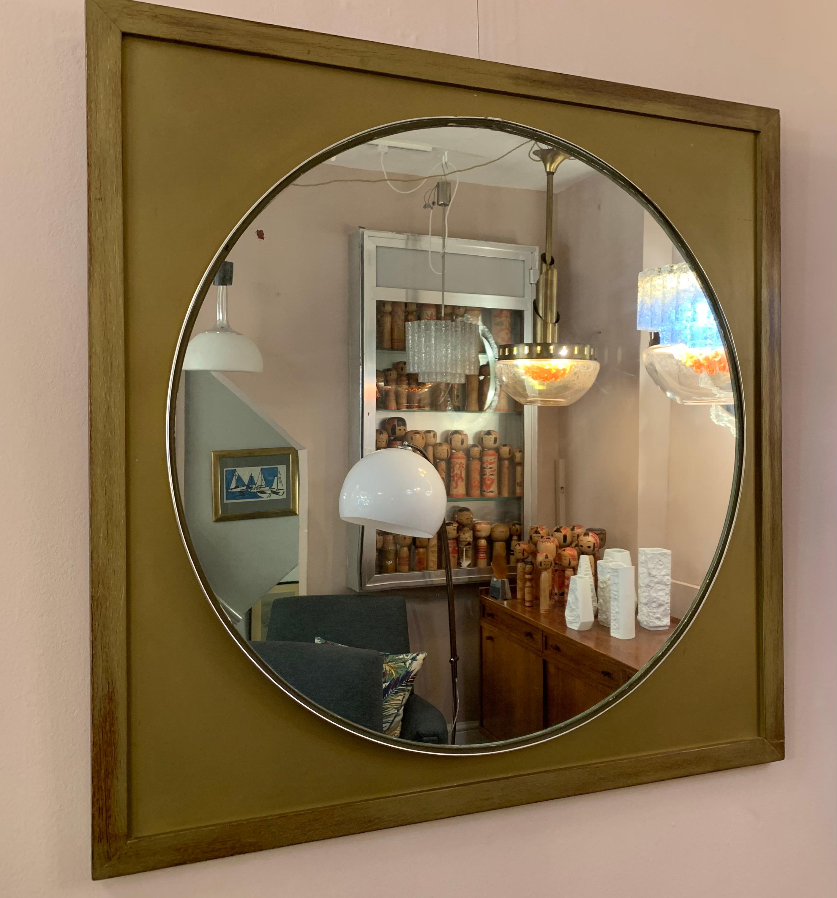 An unusual Scandinavian 1970s mid century round mirror on a wooden frame. The wooden frame is painted gold with the grain showing through on the outside edges. The circular glass mirror is surrounded a small rubber band which holds it in place in