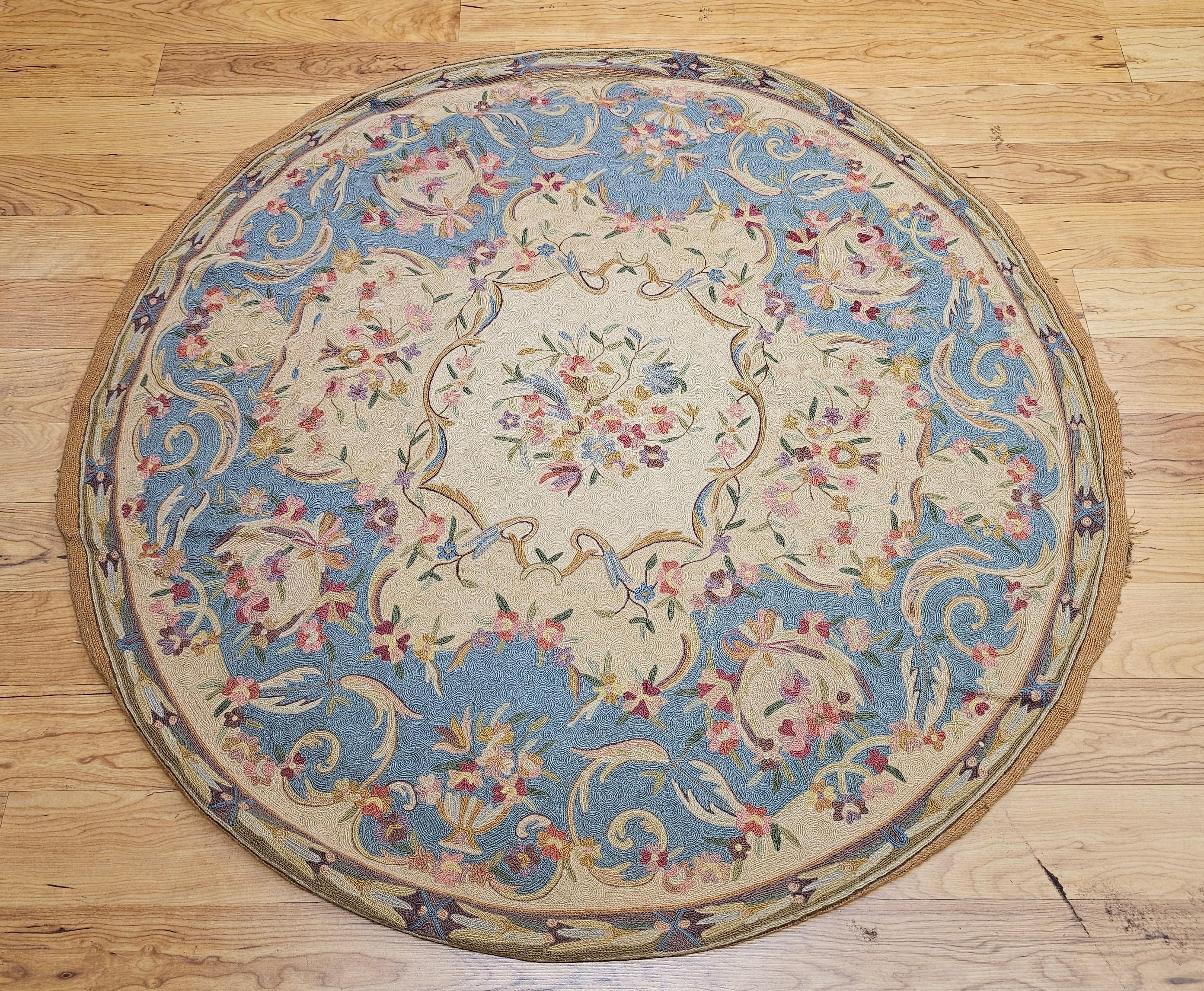 Alfombra redonda Vintage Needlepoint en azul claro, rojo, verde, marrón y marfil.  La alfombra tiene un bonito motivo floral despejado sobre un fondo de color marfil con un borde ancho en azul pálido.  Se creó hábilmente utilizando el método de