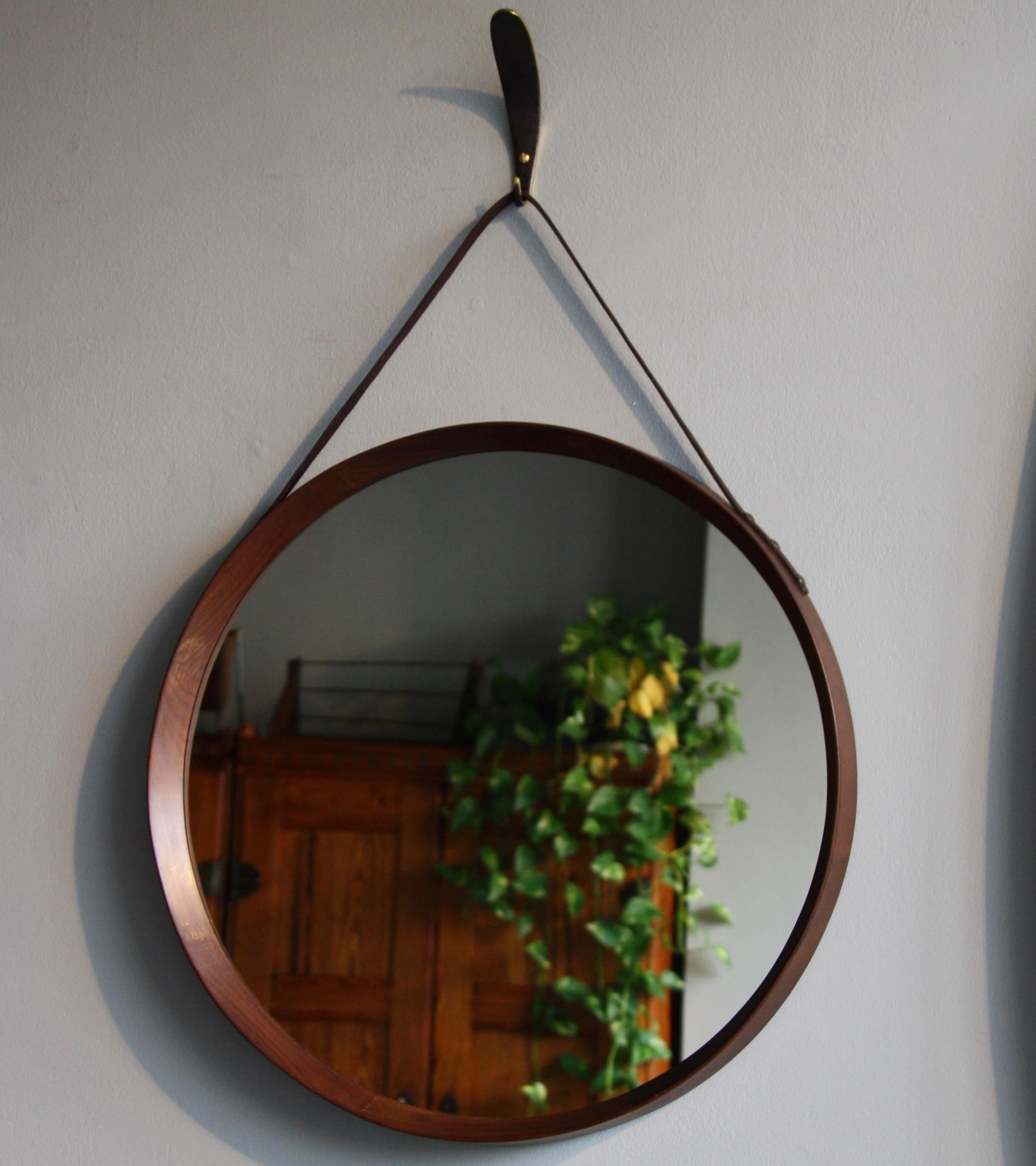 A vintage round wall mirror made in Denmark, circa 1950. The mirror is made of sections of solid teak wood which are joined together using finger joints. This exposed construction and the tapering of the wood towards the front of the mirror are the
