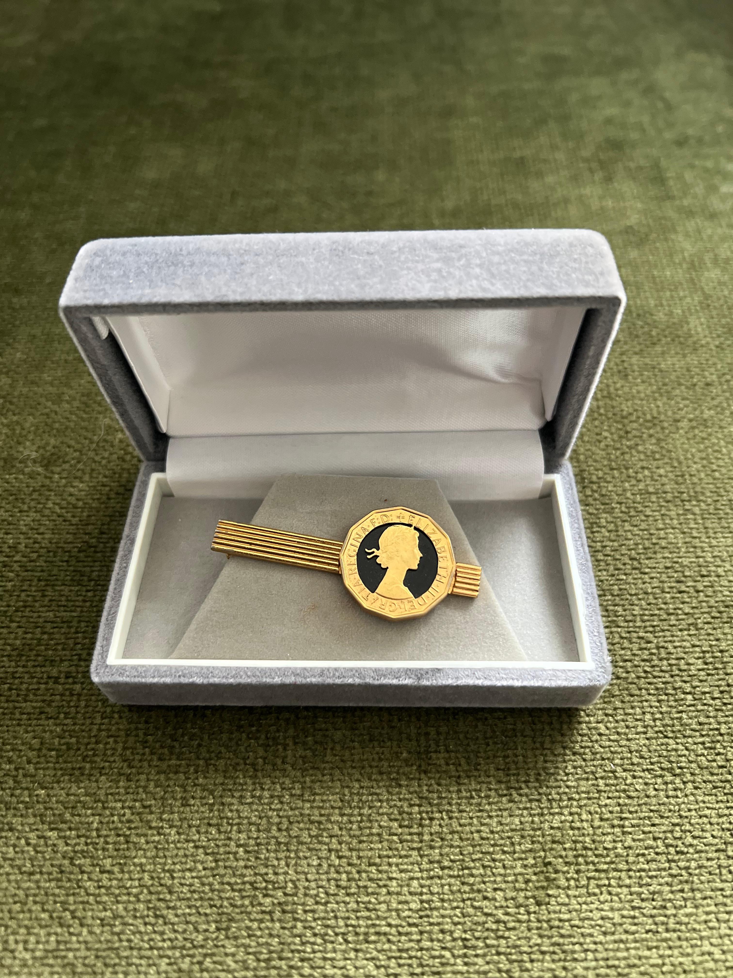 Fermacravatte d'epoca con monete placcate in oro della Royal British nella custodia originale CIRCA 1970

The tie clip in is a vintage gold-toned piece featuring a coin-style medallion with the profile of Queen Elizabeth II, resembling a British or