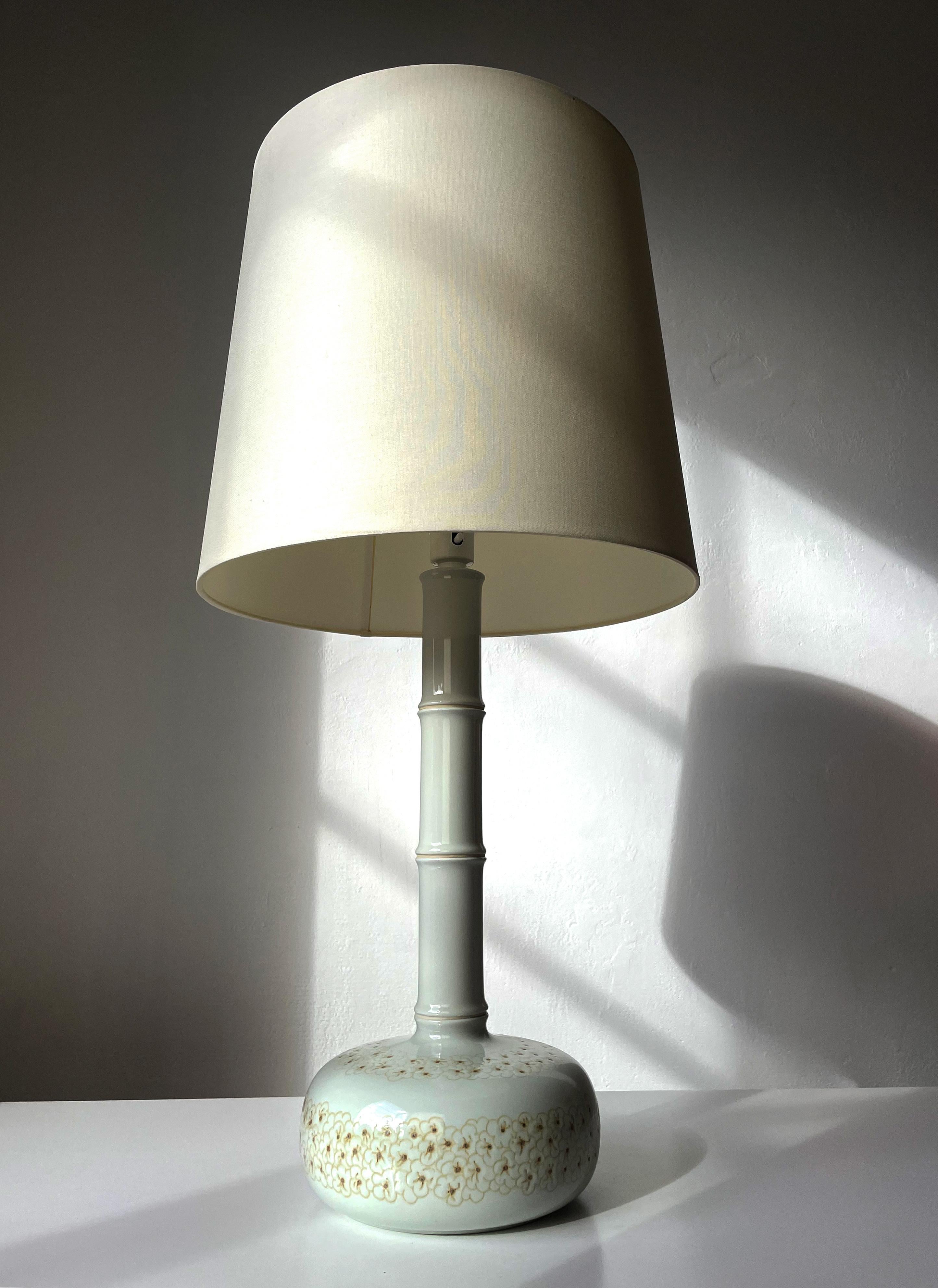 Tall Danish organic modernist faience Royal Copenhagen table lamp manufactured in the late 1960s. Shiny warm light grey glaze. Large round base with hand-carved and handpainted relief stylized flowers in yellow and curry ochre colors. Long slender