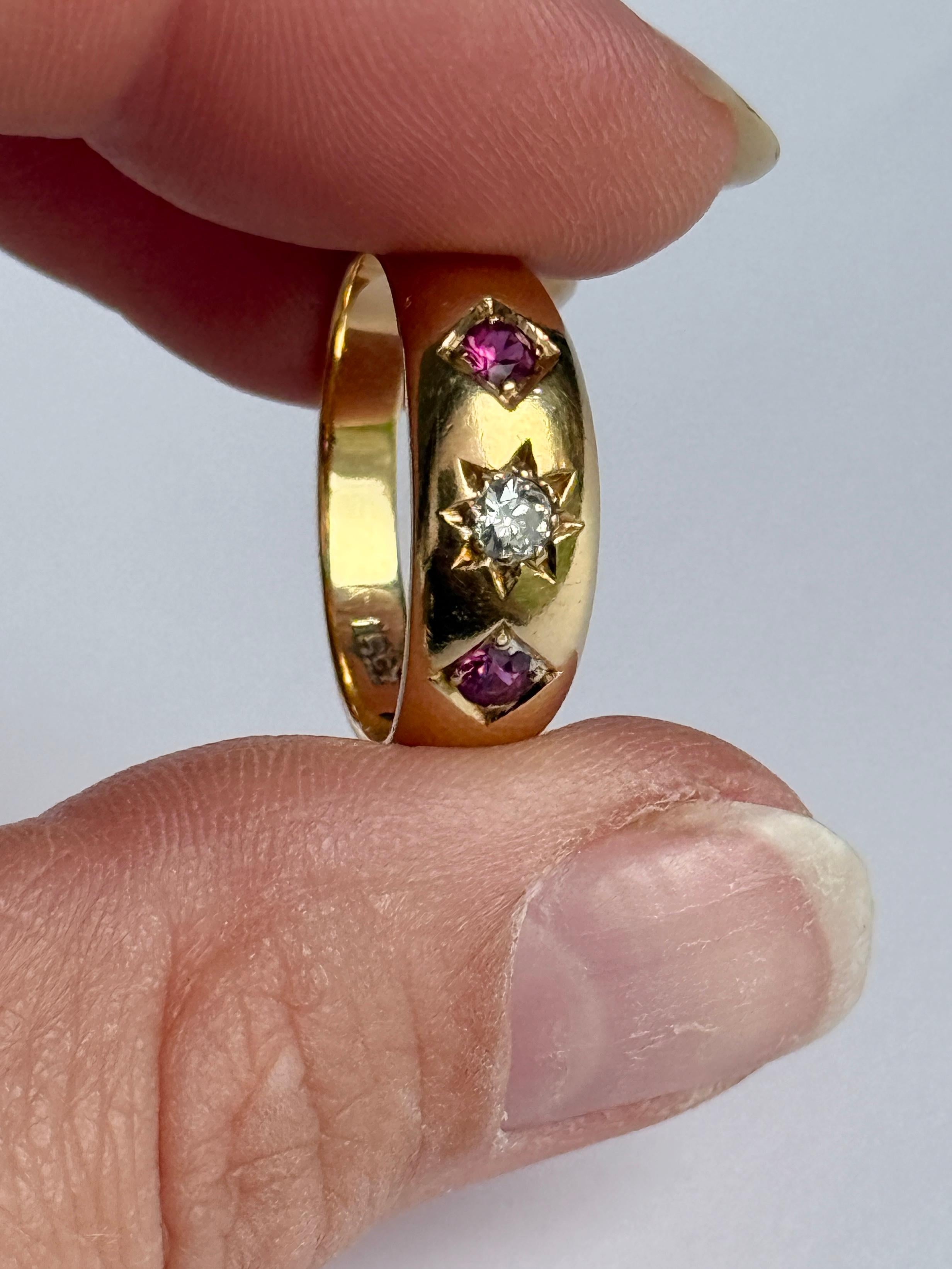 The central diamond in this glossy 18ct gold band measures 15pts. The rubies that sit either side of this stone measure 8pts each.

Ring Size: N 1/2 or 7 
Band Width: 7mm 

Weight: 4.5g 