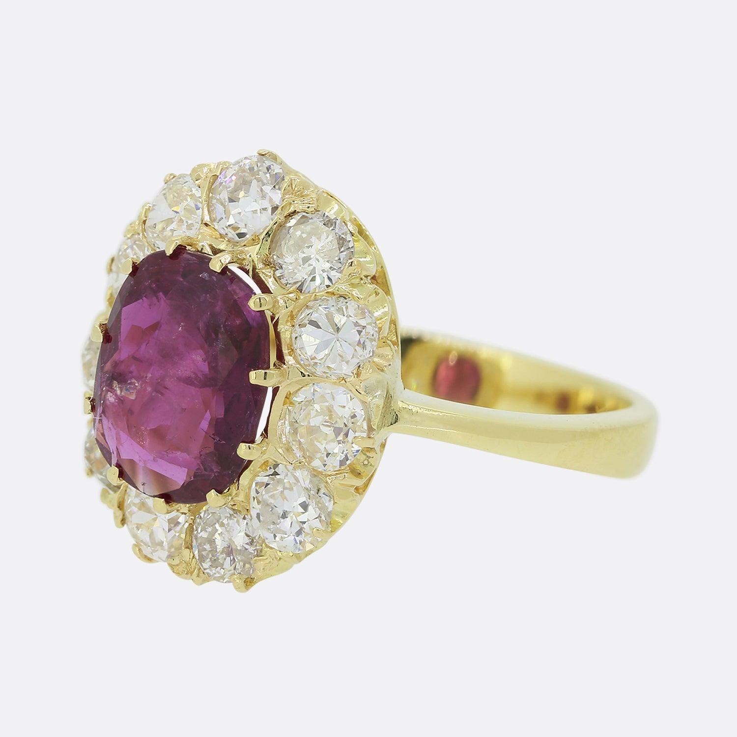 This is an 18ct yellow gold ruby and diamond cluster ring. The ring features a central oval cushion cut ruby surrounded by eleven old cut diamonds. The diamonds feature a bright white sparkle which highly compliments the dark red tone of the ruby.