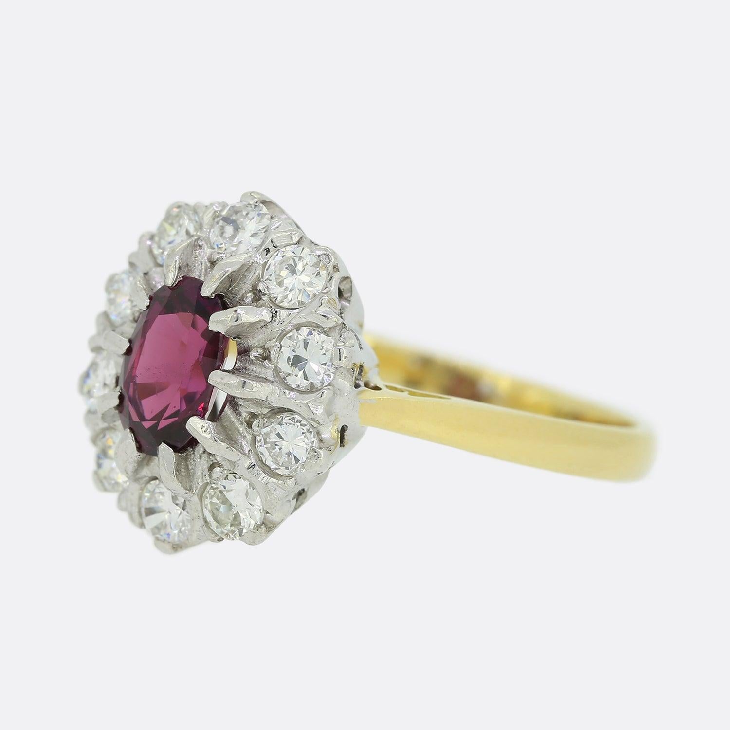 Here we have a vintage 18ct yellow gold ruby and diamond cluster ring. This piece presents a deep toned oval shaped ruby at the centre which is encompassed by an array of round brilliant cut diamonds that circulate the outer edge in white gold.