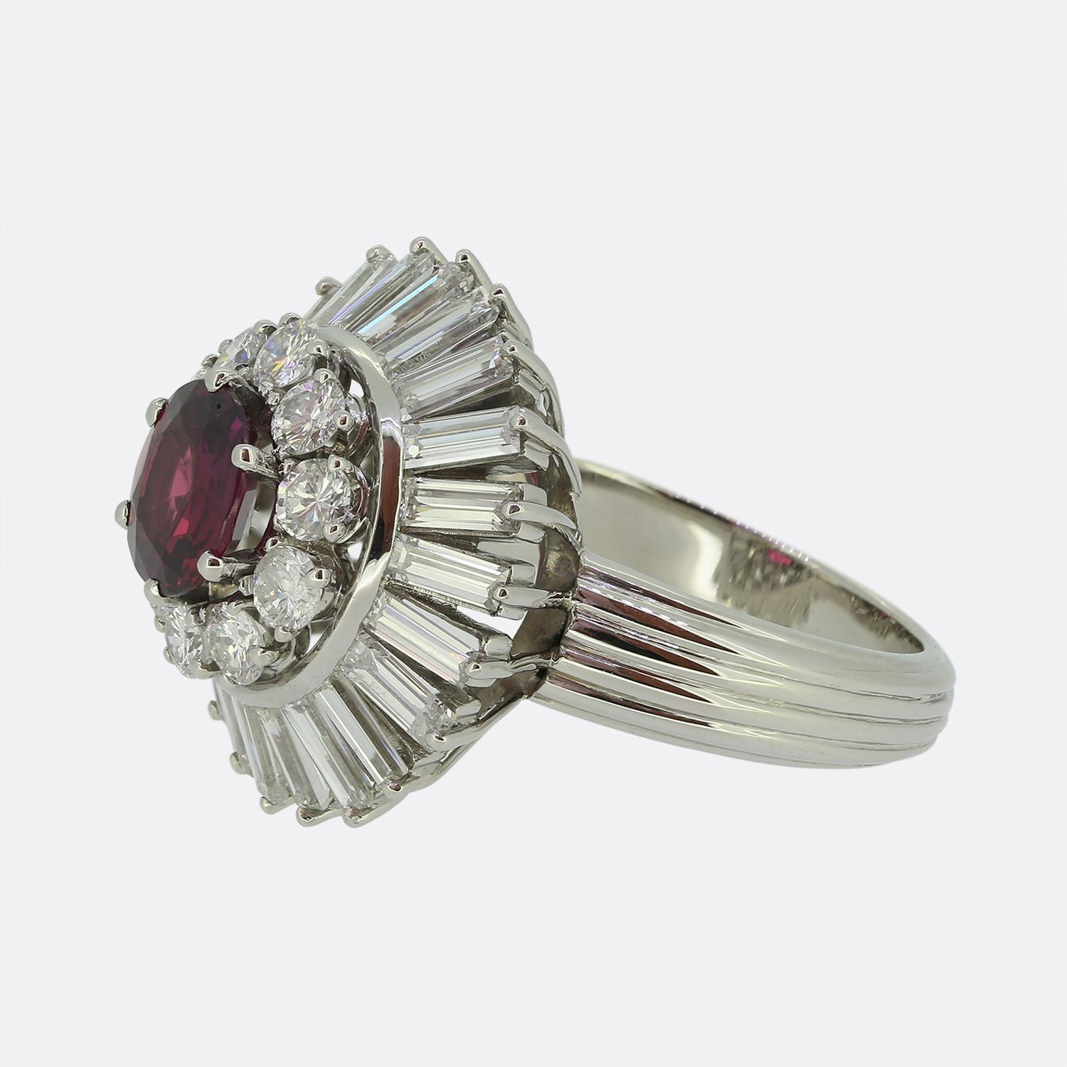 Hier haben wir einen bemerkenswerten Clusterring, der sorgfältig aus Platin gefertigt wurde. Sein Herzstück ist ein bezaubernder Rubin, der einen tiefroten Farbton ausstrahlt. Dieser Hauptstein wird von einem Halo aus funkelnden runden Diamanten im